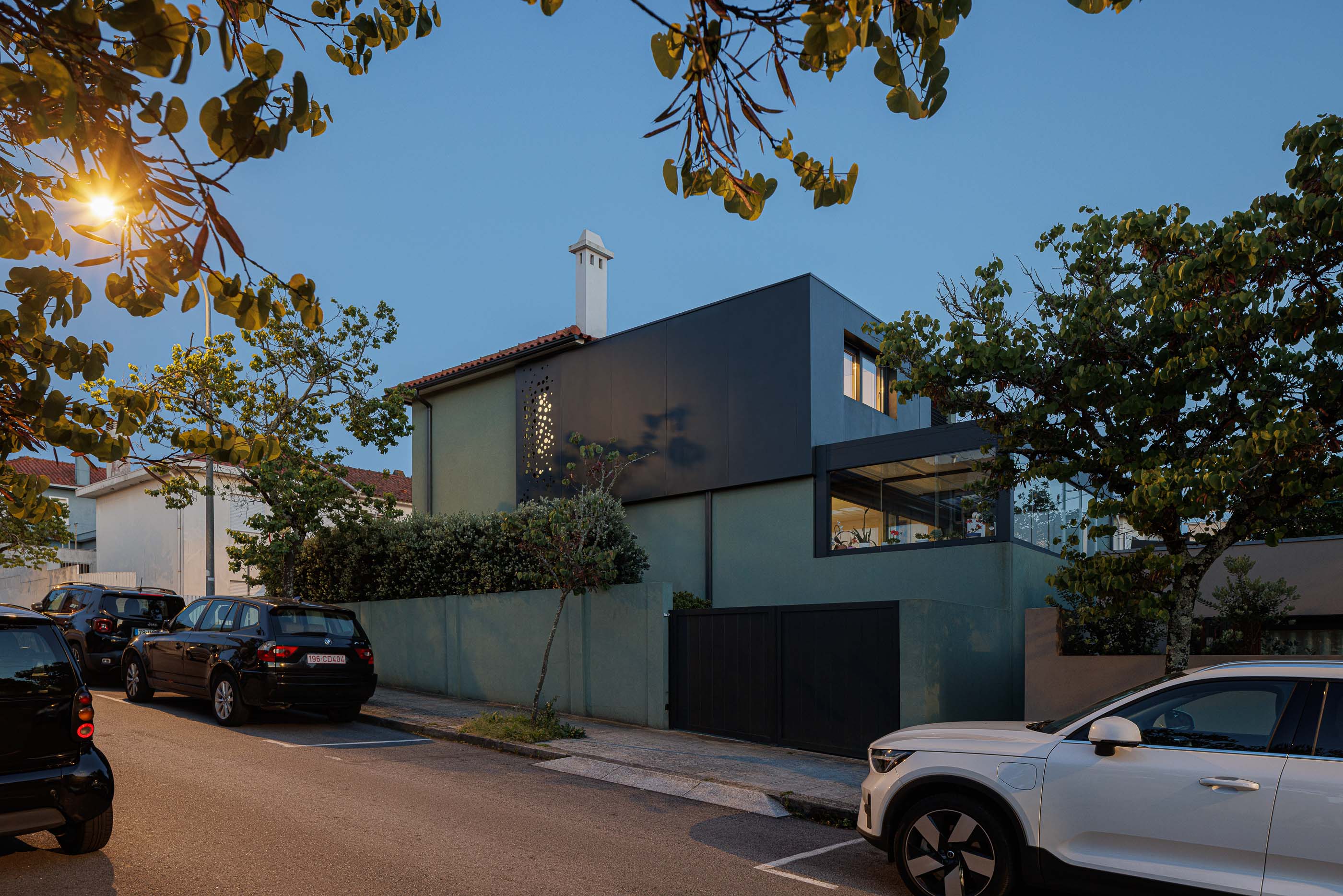 Fachada: Detalhe da fachada verde com janelas iluminadas e vegetação densa. — Casa Pi arquitetura ArquitectosRT em Porto