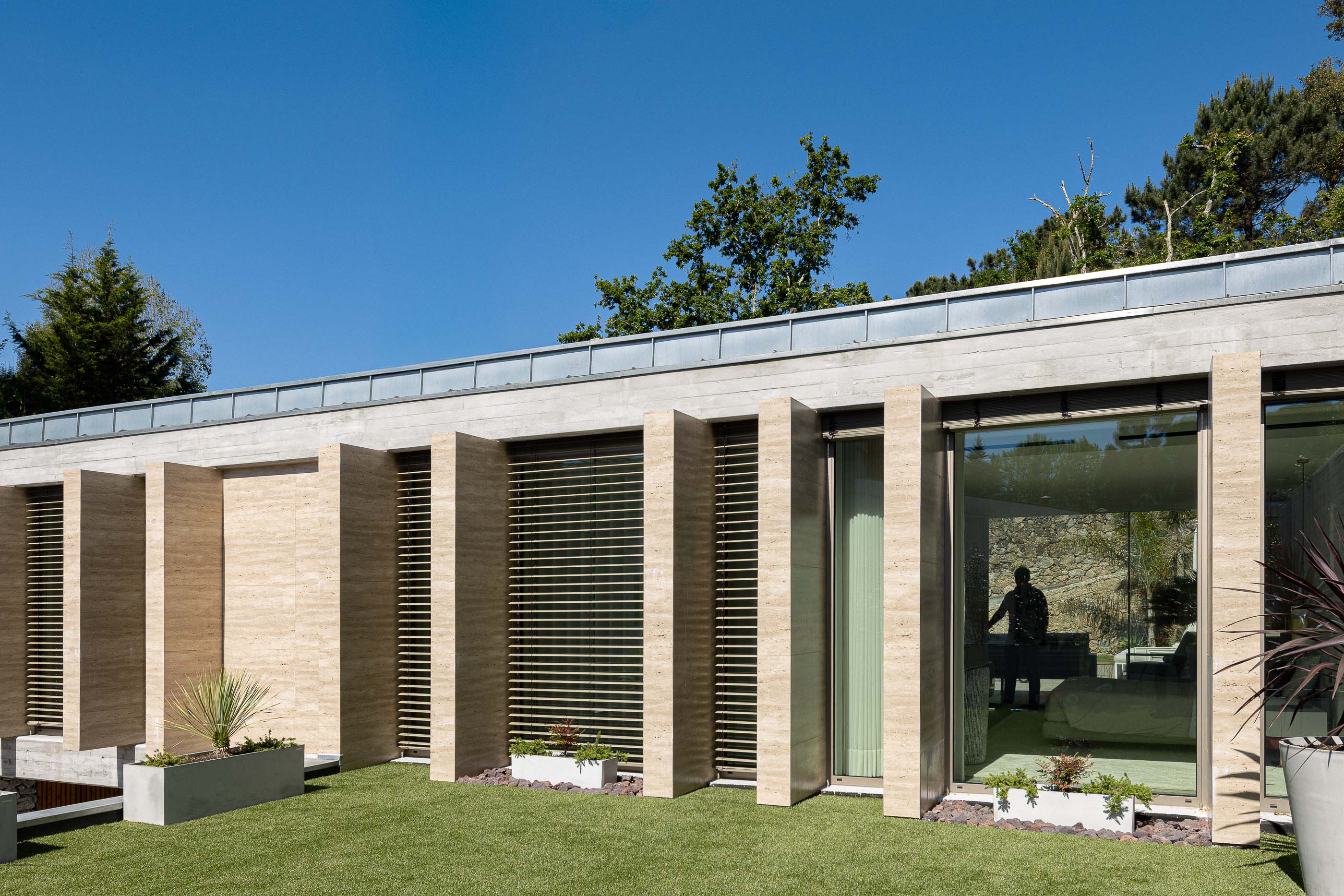 Jardim: Fachada com elementos verticais em betão, relvado e vasos com plantas. — Habitação CL arquitetura Artequitectos em Guimarães