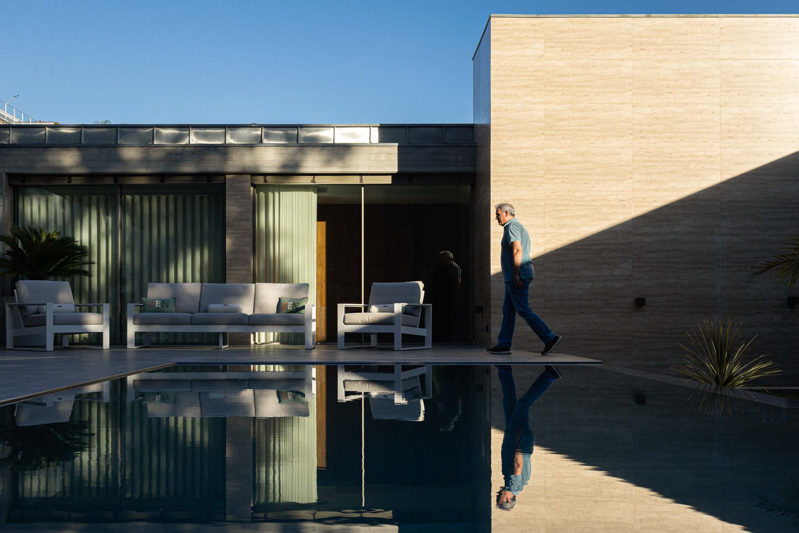 Exterior: Piscina com reflexo da fachada em betão e zona de estar. — Habitação CL arquitetura Artequitectos em Guimarães