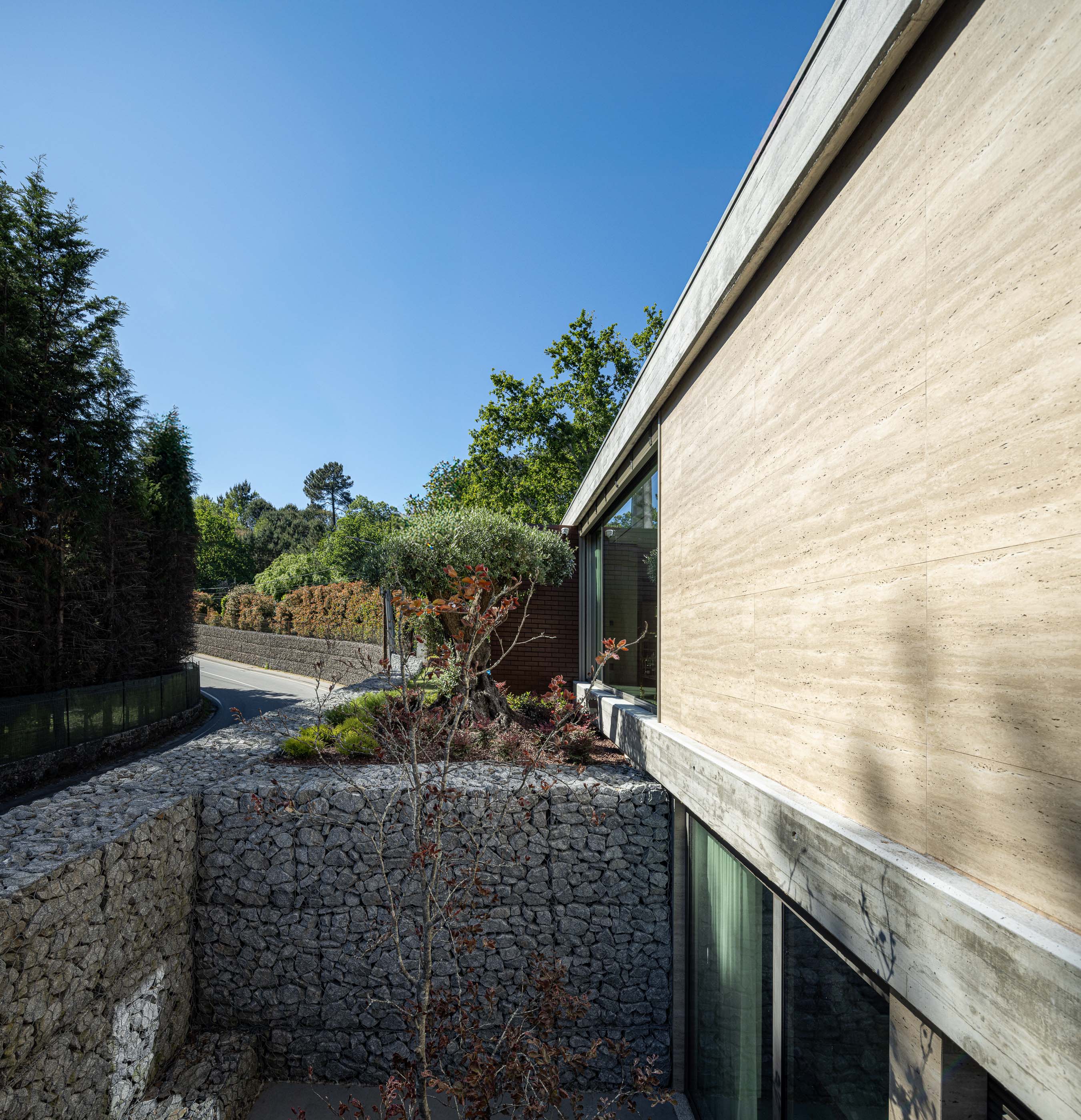 Exterior: Vista lateral da casa com muro em pedra e jardim. — Habitação CL arquitetura Artequitectos em Guimarães