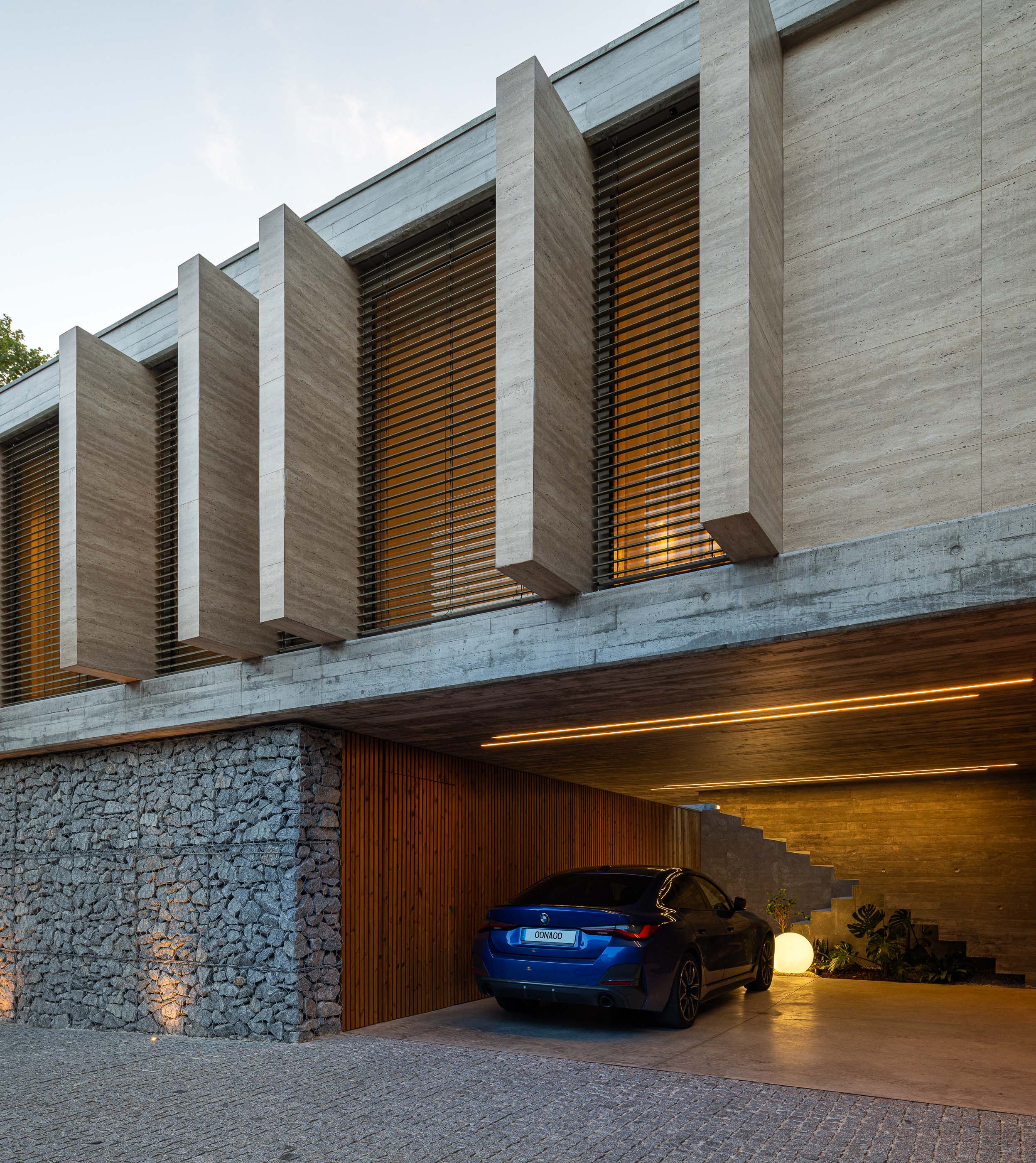 Entrada: Vista noturna da entrada da casa com garagem, iluminação e fachada em betão. — Habitação CL arquitetura Artequitectos em Guimarães