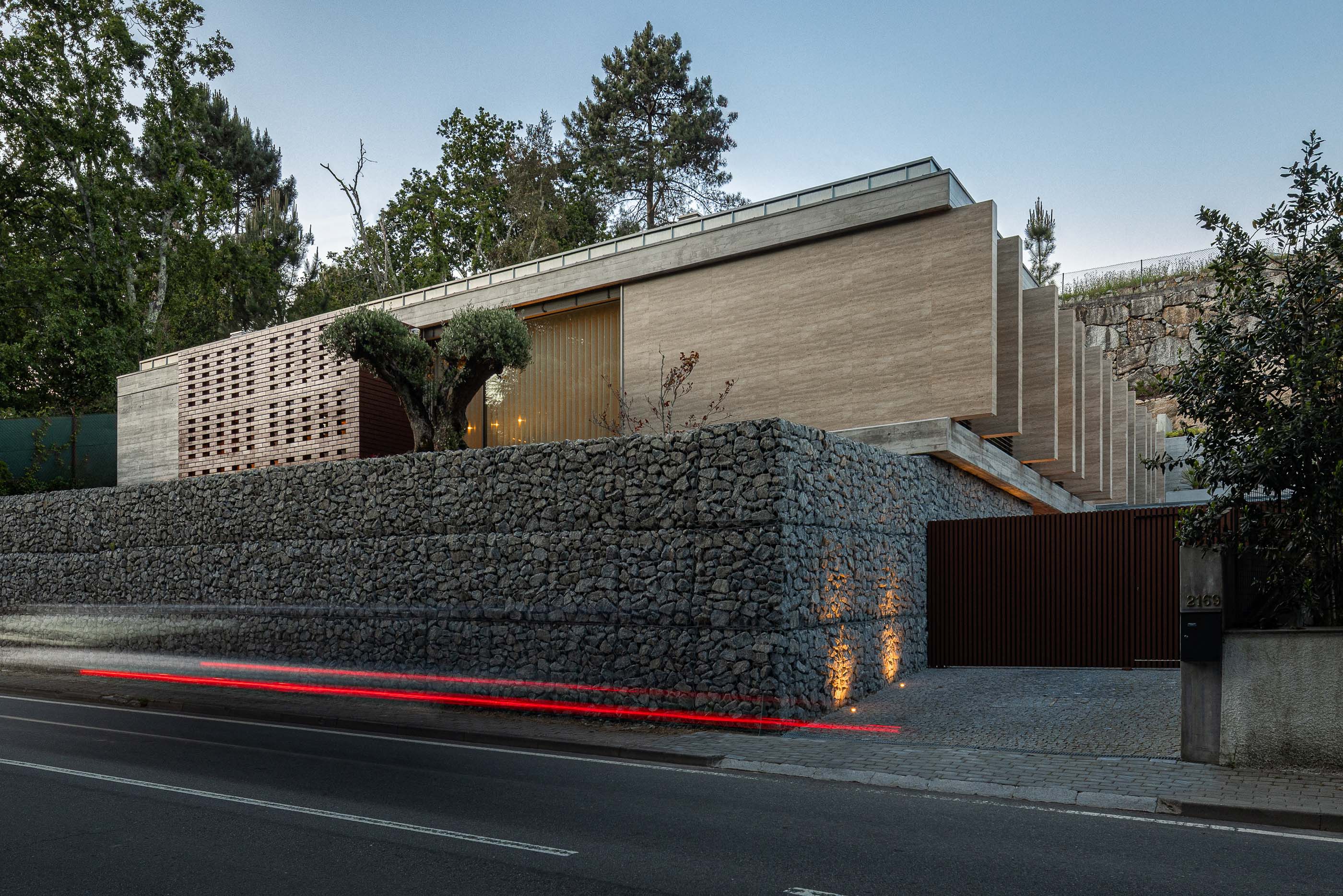 Exterior: Vista noturna da casa com muro em pedra e iluminação exterior. — Habitação CL arquitetura Artequitectos em Guimarães