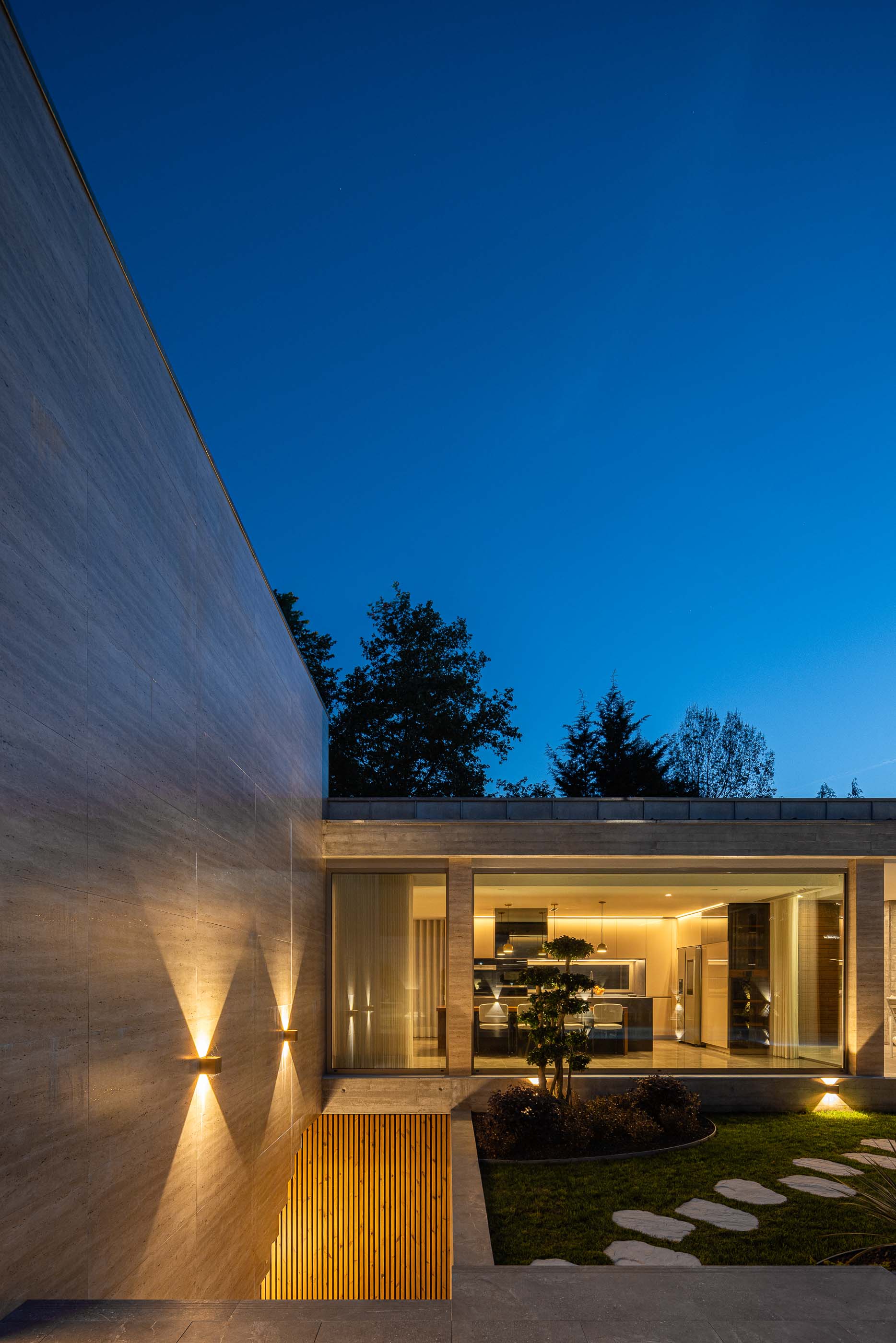 Exterior: Vista noturna da fachada com cozinha iluminada e jardim. — Habitação CL arquitetura Artequitectos em Guimarães