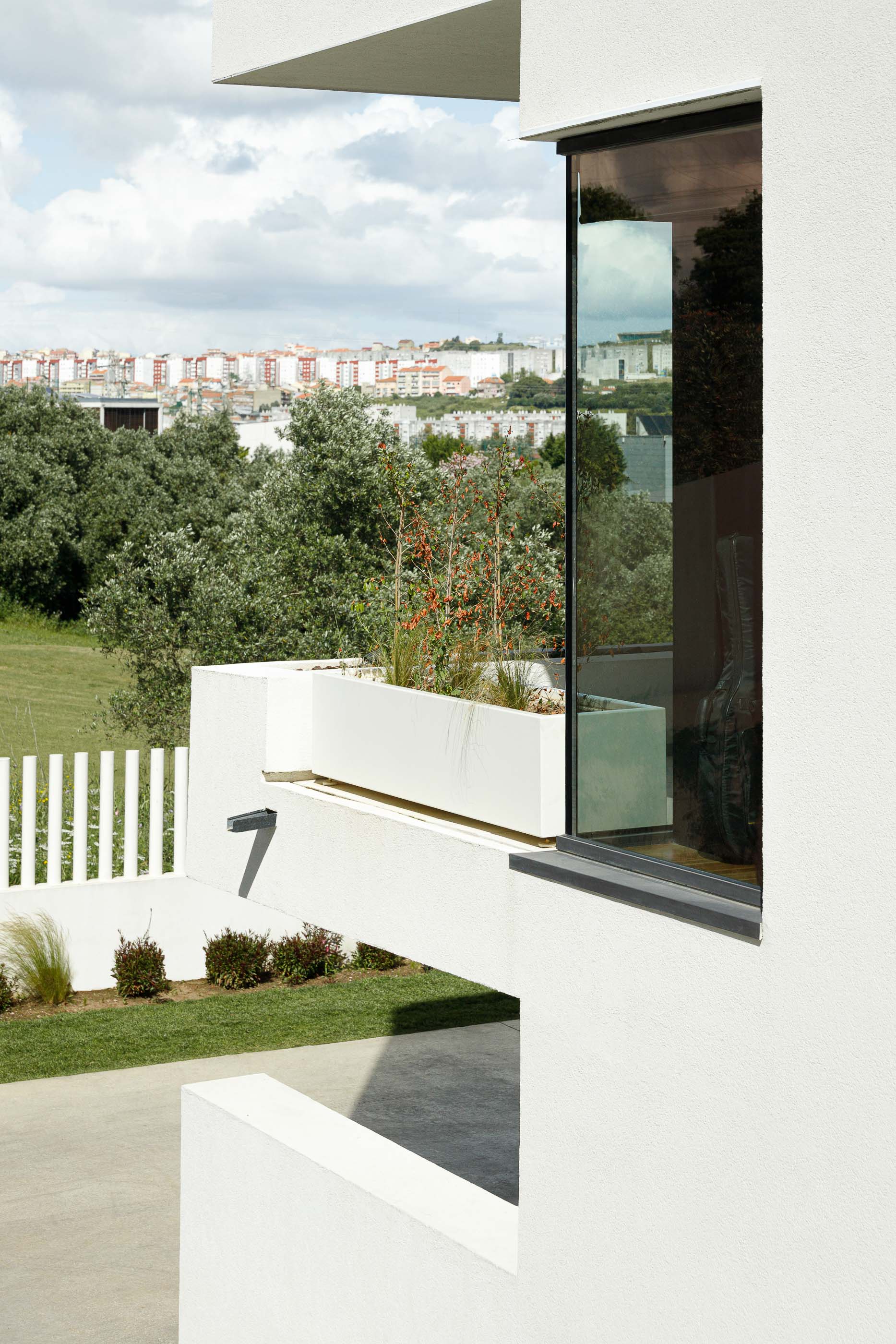 Exterior: Detalhe da fachada branca com janela envidraçada, floreira e vegetação circundante. — Casa dos Alcoutins arquitetura Paulo Martins Arquitectura e Design em Lisboa
