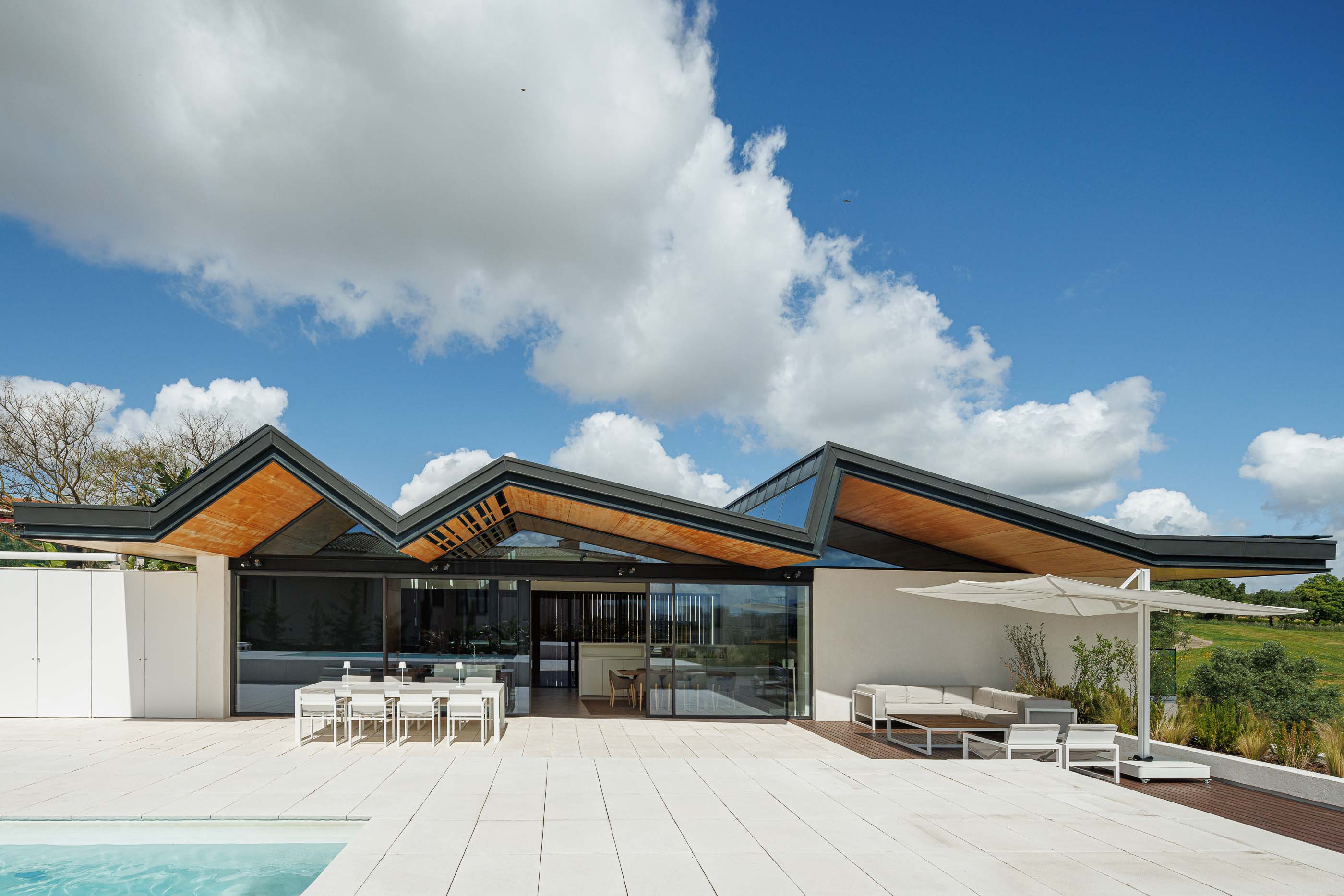Terraço: Vista geral do terraço com piscina, zona de estar, mesa de jantar e telhado angular. — Casa dos Alcoutins arquitetura Paulo Martins Arquitectura e Design em Lisboa