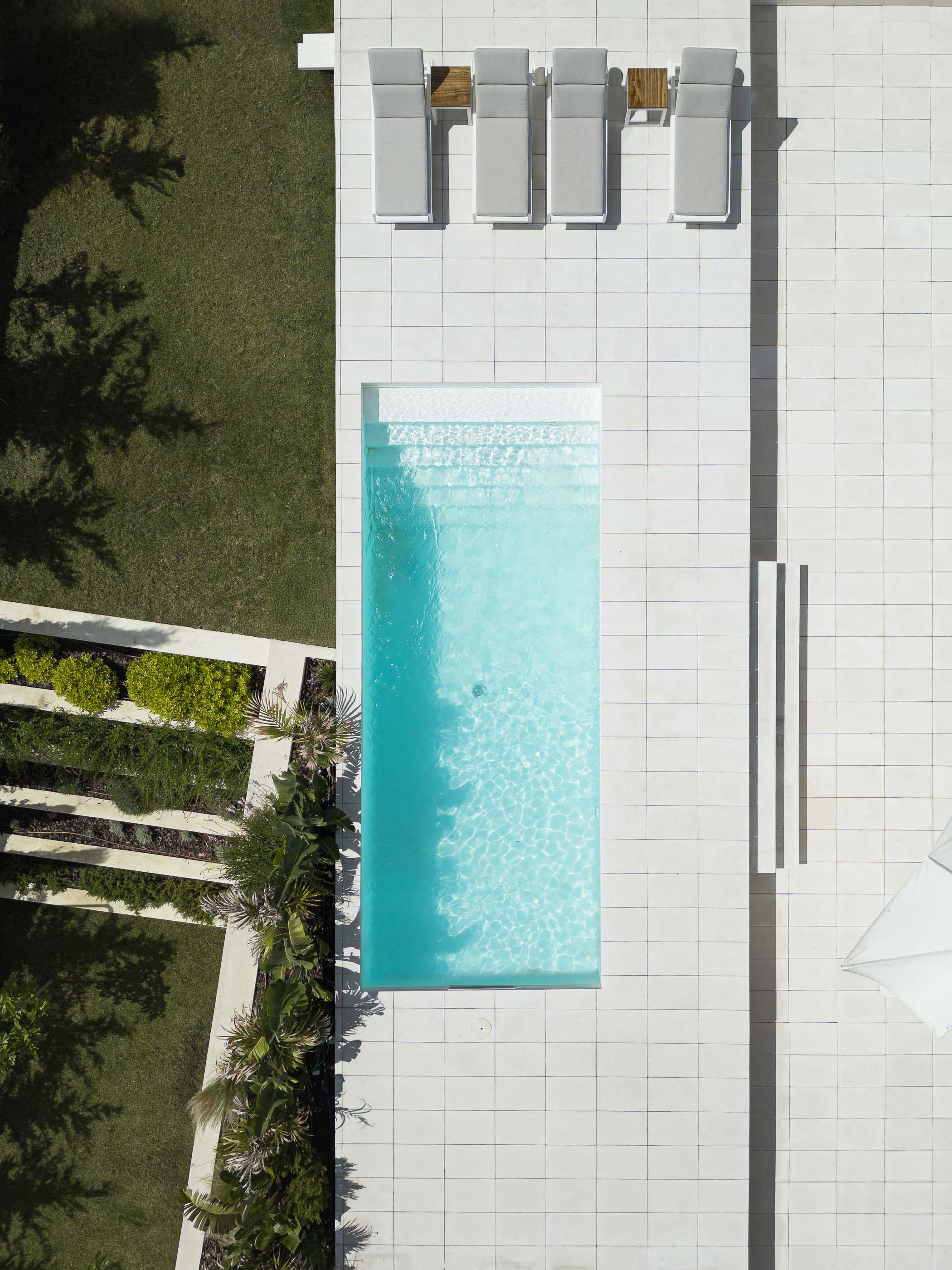 Piscina: Vista aérea da piscina retangular com espreguiçadeiras, jardim e pavimento em pedra clara. — Casa dos Alcoutins arquitetura Paulo Martins Arquitectura e Design em Lisboa
