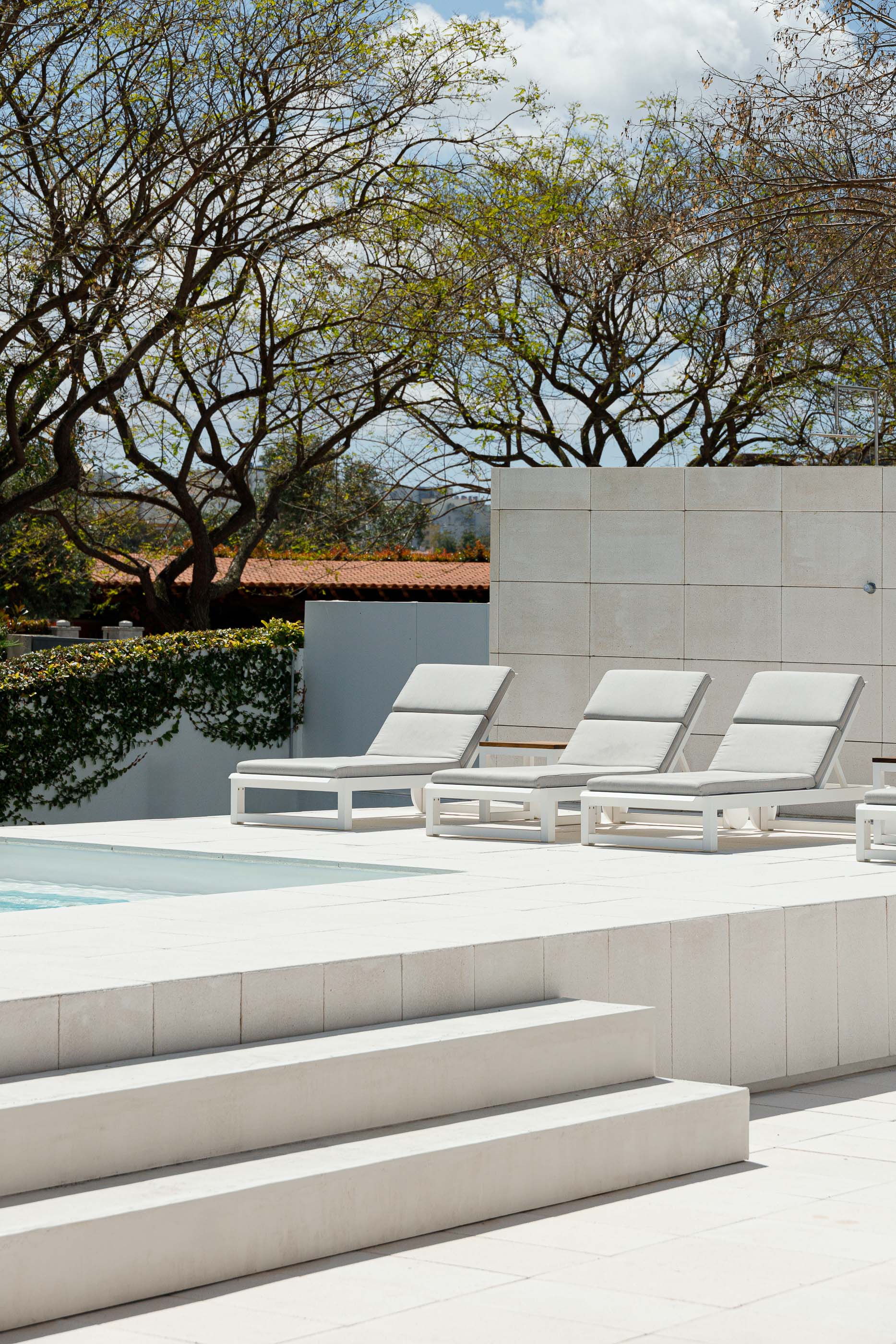 Piscina: Detalhe da área da piscina com espreguiçadeiras e parede revestida a pedra clara. — Casa dos Alcoutins arquitetura Paulo Martins Arquitectura e Design em Lisboa