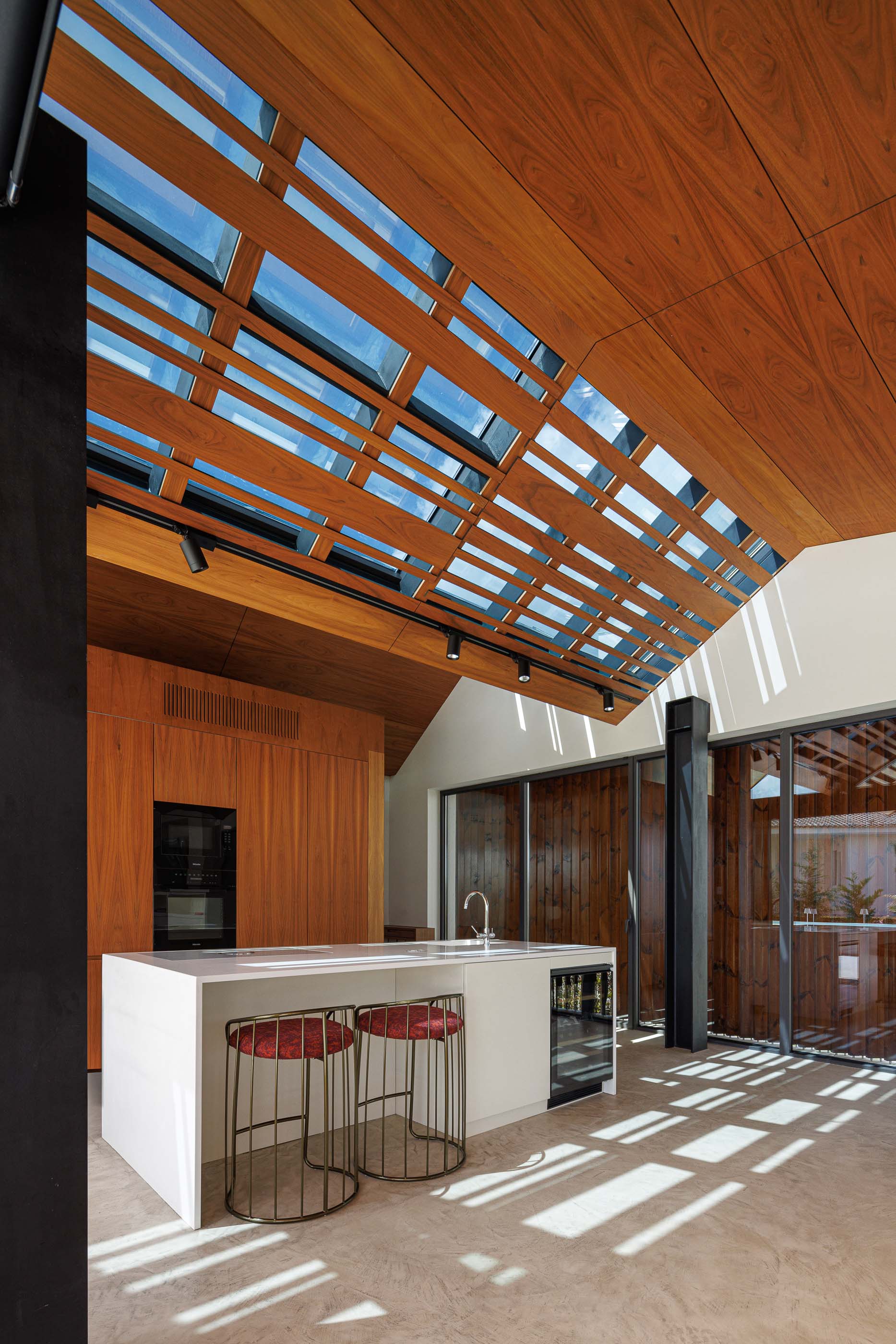 Cozinha: Detalhe do teto em madeira com claraboias, bancada branca e cadeiras altas. — Casa dos Alcoutins arquitetura Paulo Martins Arquitectura e Design em Lisboa