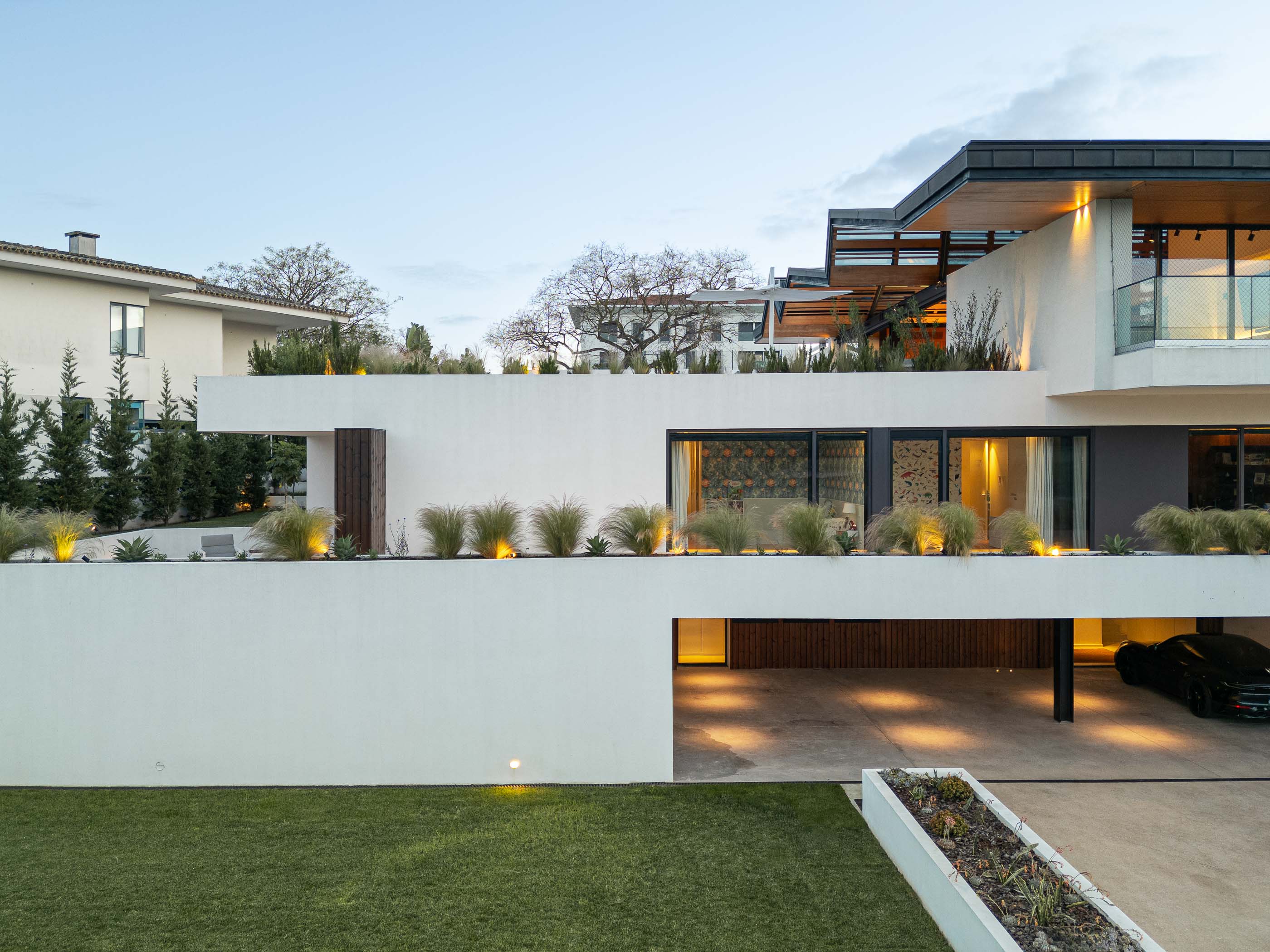 Exterior: Vista noturna da casa com piscina, terraço iluminado e telhado angular. — Casa dos Alcoutins arquitetura Paulo Martins Arquitectura e Design em Lisboa