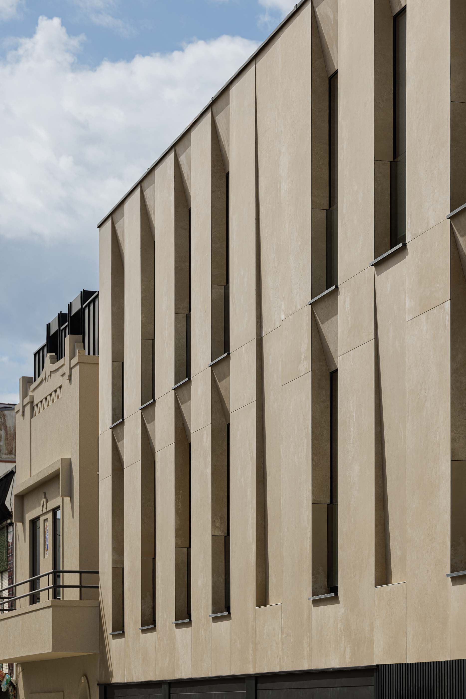 Fachada: Perspectiva lateral do edifício com janelas verticais em betão texturado. — Reabilitação Poveira - Edifício FS11 arquitetura Urbanpolis em Póvoa de Varzim