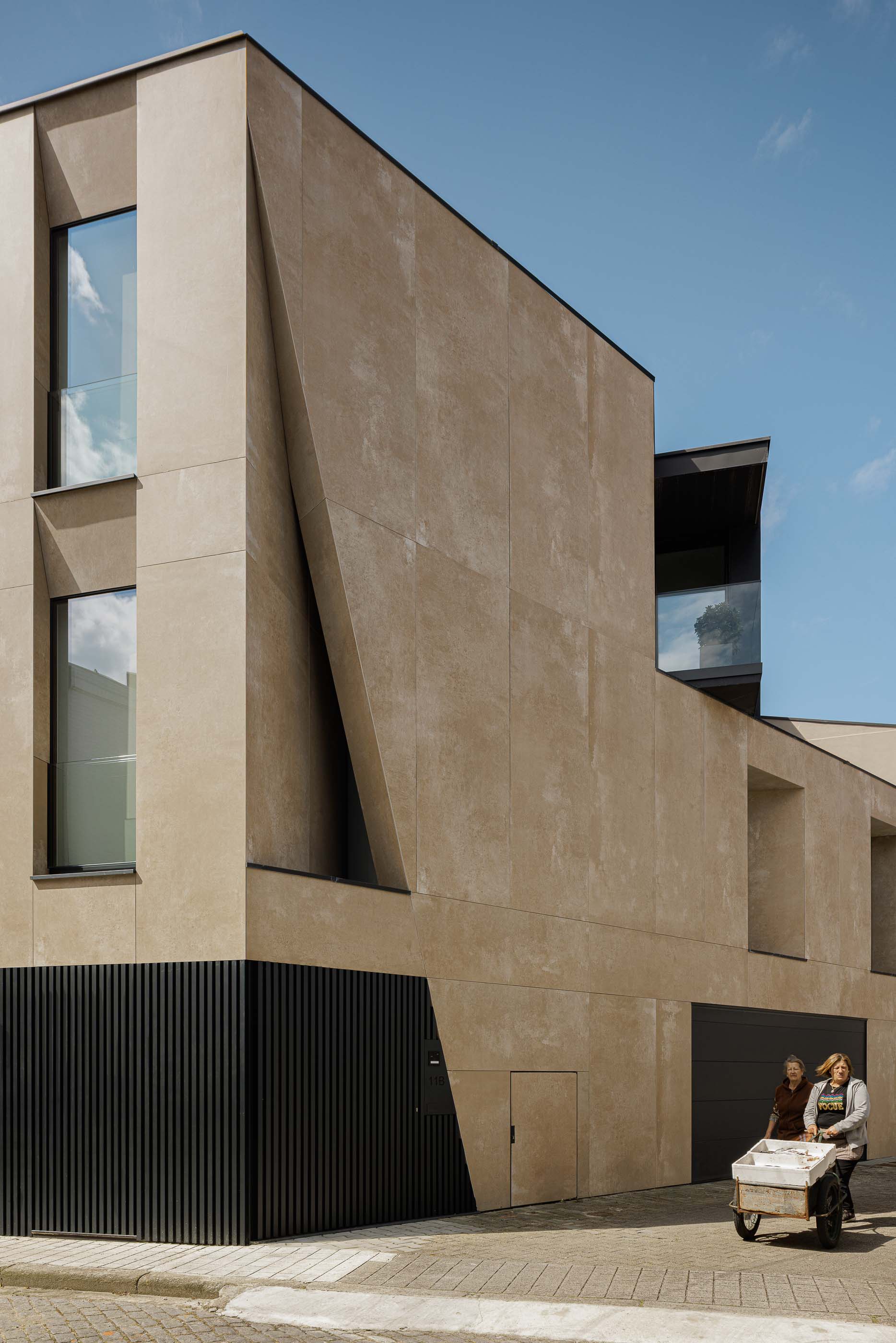 Fachada: Vista lateral do edifício com detalhes geométricos, janelas verticais e garagem. — Reabilitação Poveira - Edifício FS11 arquitetura Urbanpolis em Póvoa de Varzim