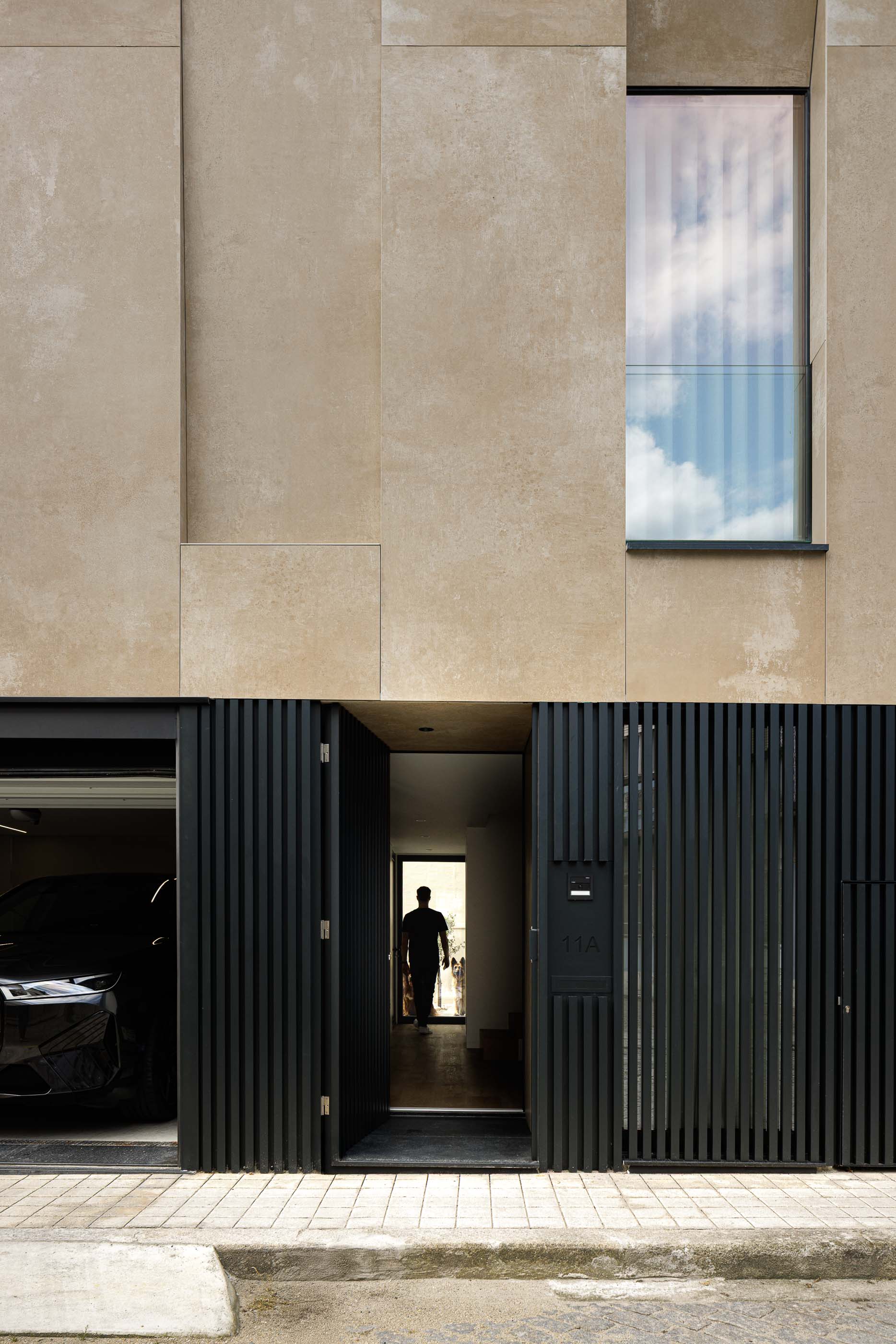 Entrada: Porta de entrada com design moderno, fachada em betão e garagem lateral. — Reabilitação Poveira - Edifício FS11 arquitetura Urbanpolis em Póvoa de Varzim