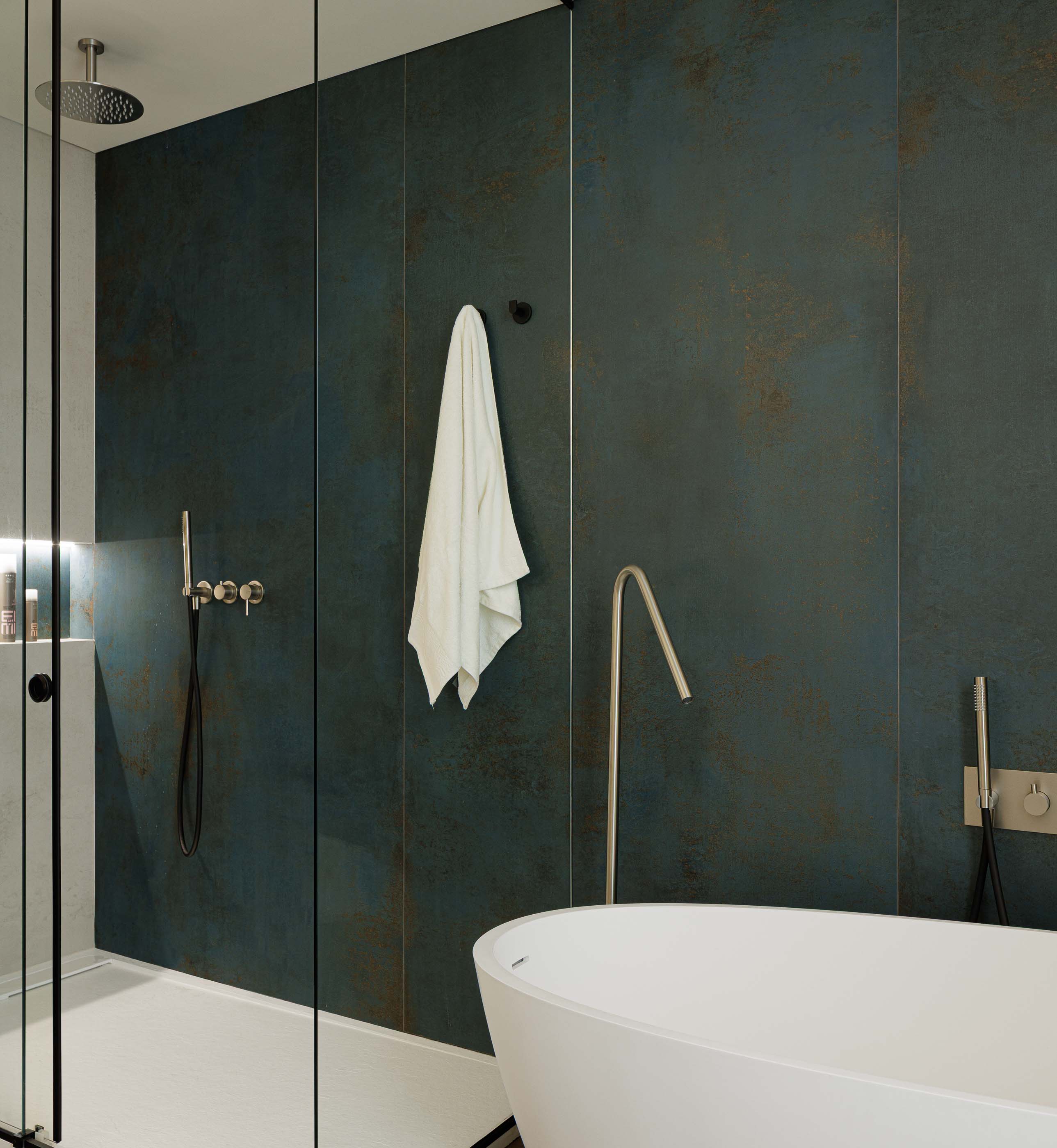 Casa de banho: Detalhe do duche com revestimento azul texturado, banheira branca e torneiras em metal. — Reabilitação Poveira - Edifício FS11 arquitetura Urbanpolis em Póvoa de Varzim