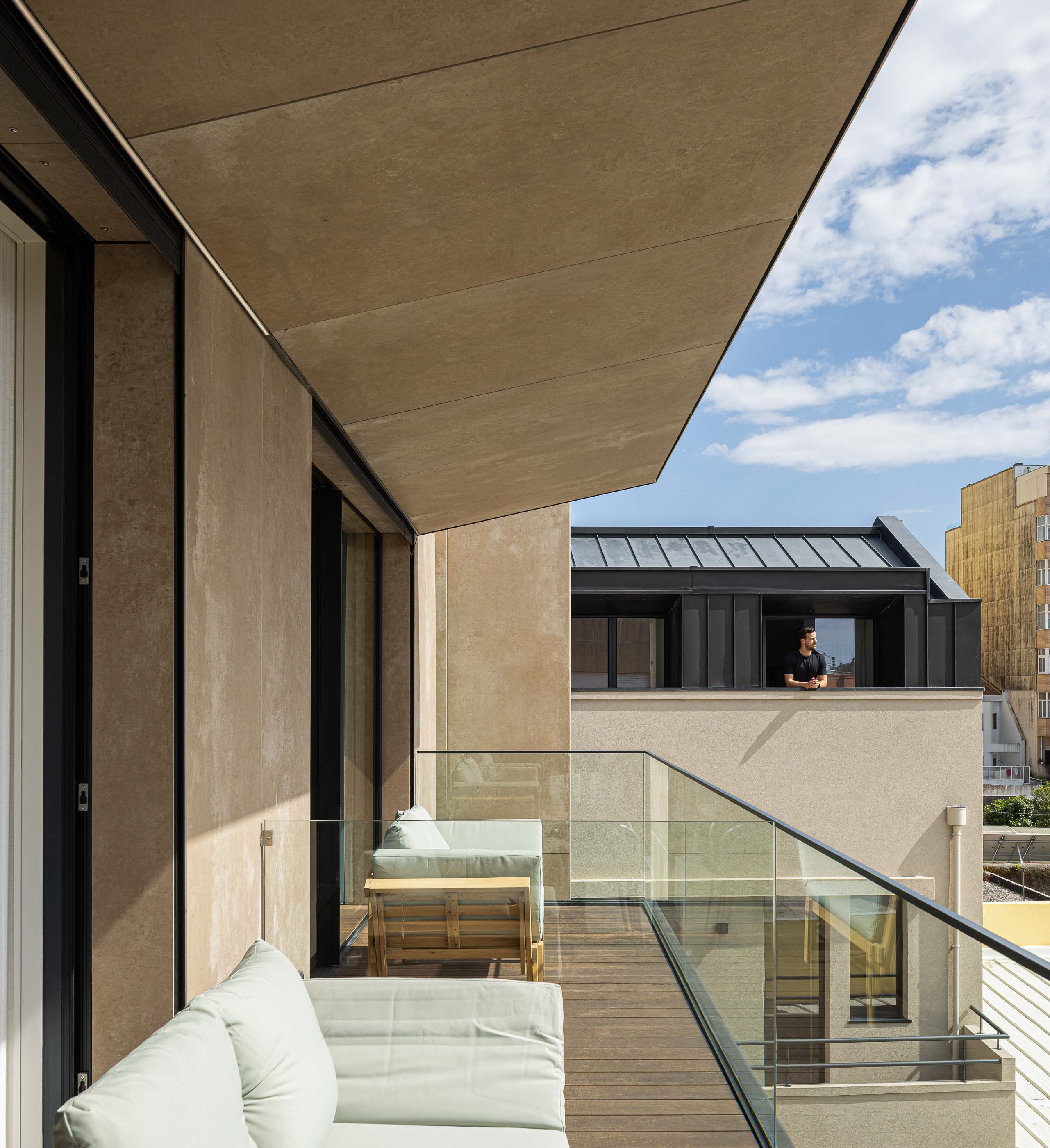 Varanda: Varanda com pavimento em madeira, sofás claros e vista para o exterior. — Reabilitação Poveira - Edifício FS11 arquitetura Urbanpolis em Póvoa de Varzim