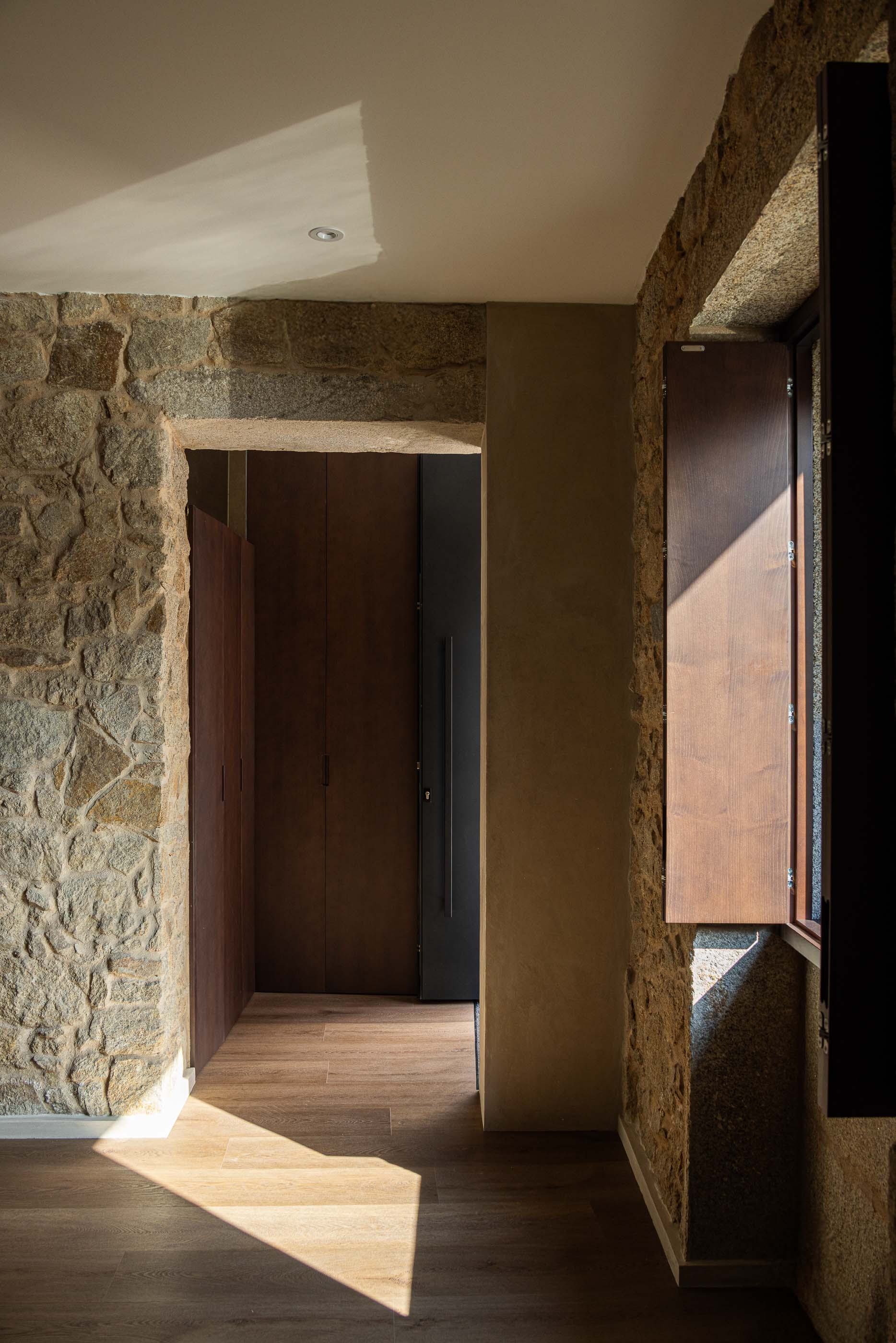 Hall de entrada: Paredes em pedra original, pavimento em madeira e porta em madeira escura. — Reabilitação Poveira - Edifício FS11 arquitetura Urbanpolis em Póvoa de Varzim