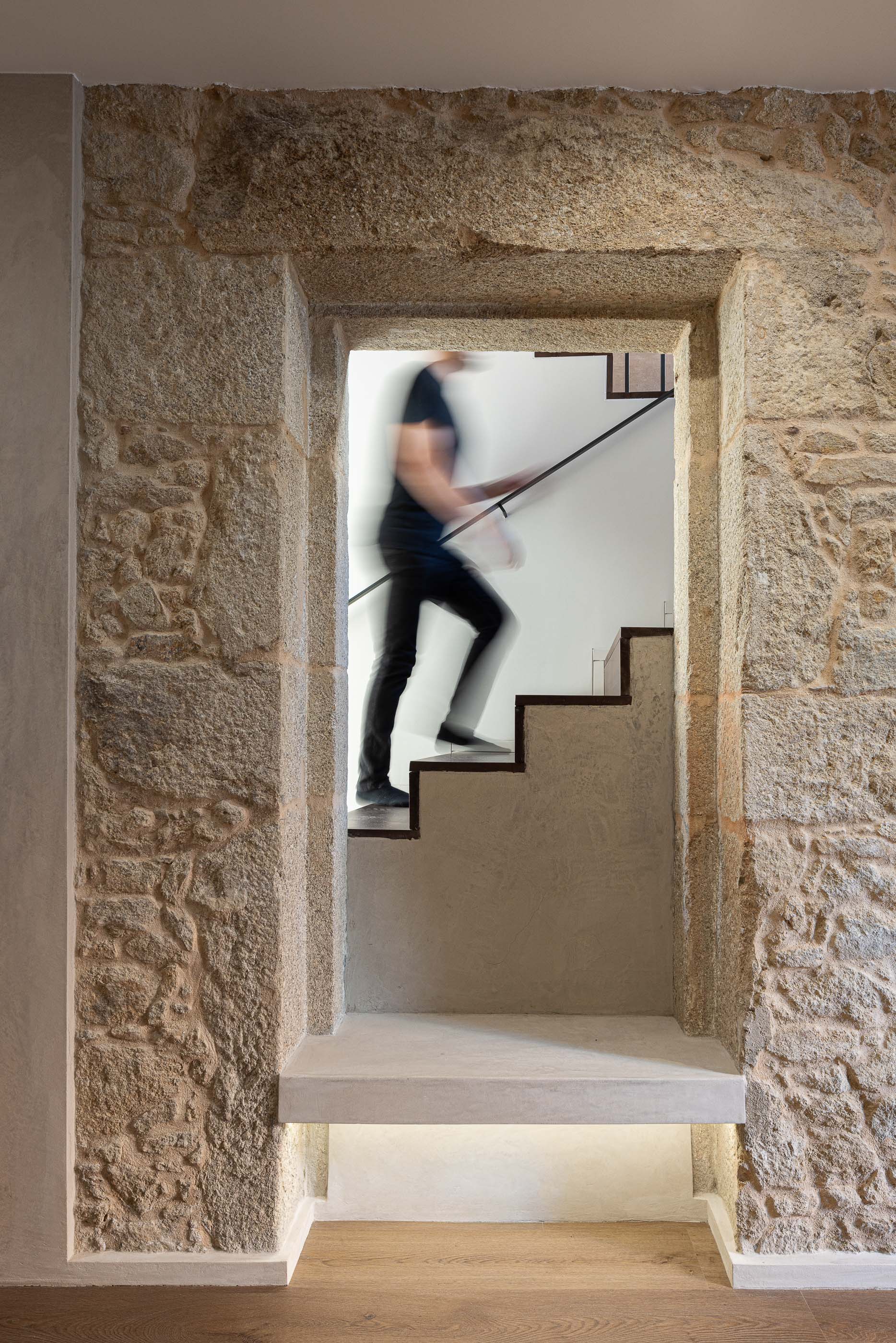 Escada: Detalhe da escada em pedra original com degraus em madeira e parede branca. — Reabilitação Poveira - Edifício FS11 arquitetura Urbanpolis em Póvoa de Varzim