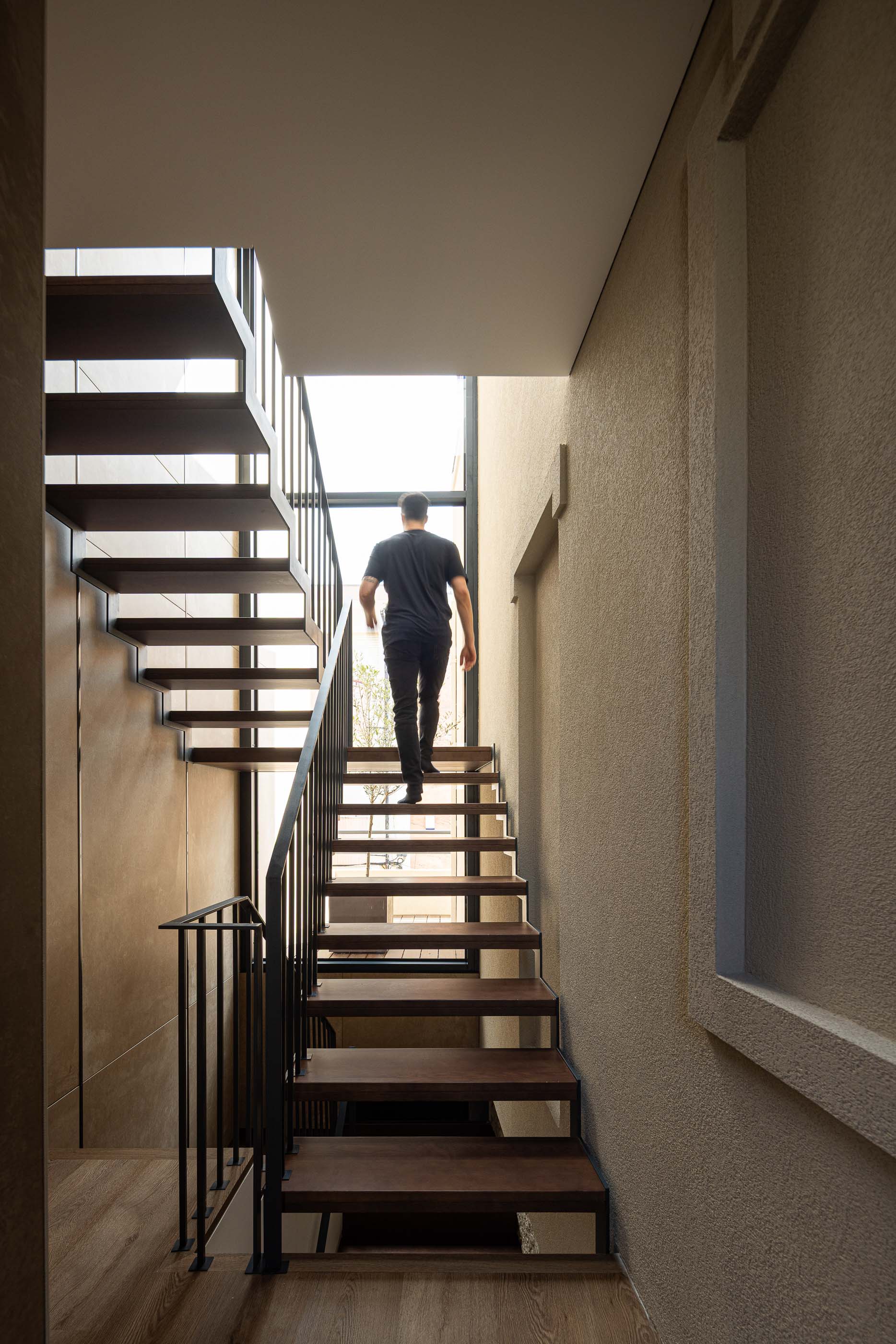 Escada: Escada moderna com degraus em madeira, grade metálica e parede em tons terra. — Reabilitação Poveira - Edifício FS11 arquitetura Urbanpolis em Póvoa de Varzim