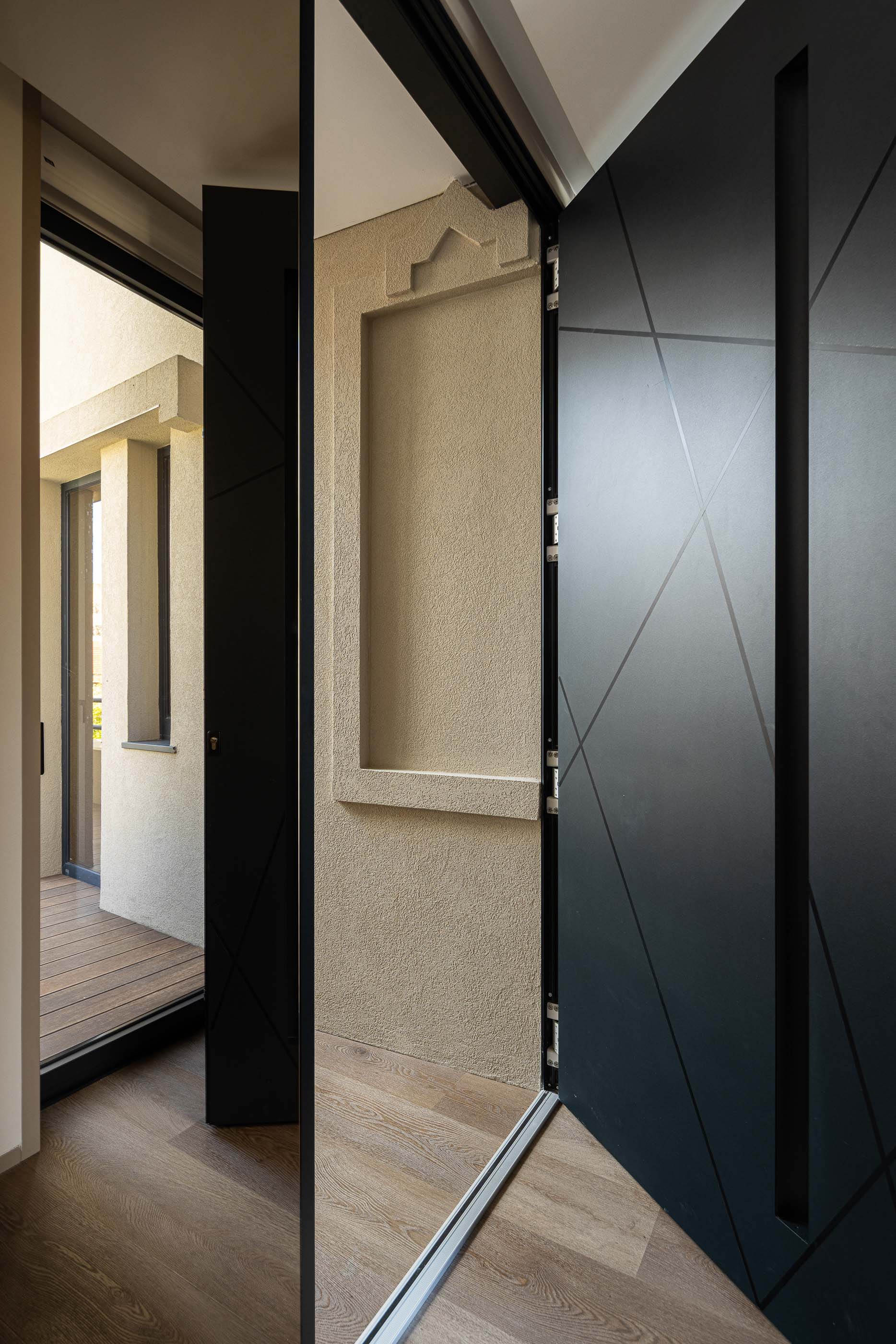 Hall de entrada: Porta preta com design geométrico, parede texturada e acesso à varanda. — Reabilitação Poveira - Edifício FS11 arquitetura Urbanpolis em Póvoa de Varzim