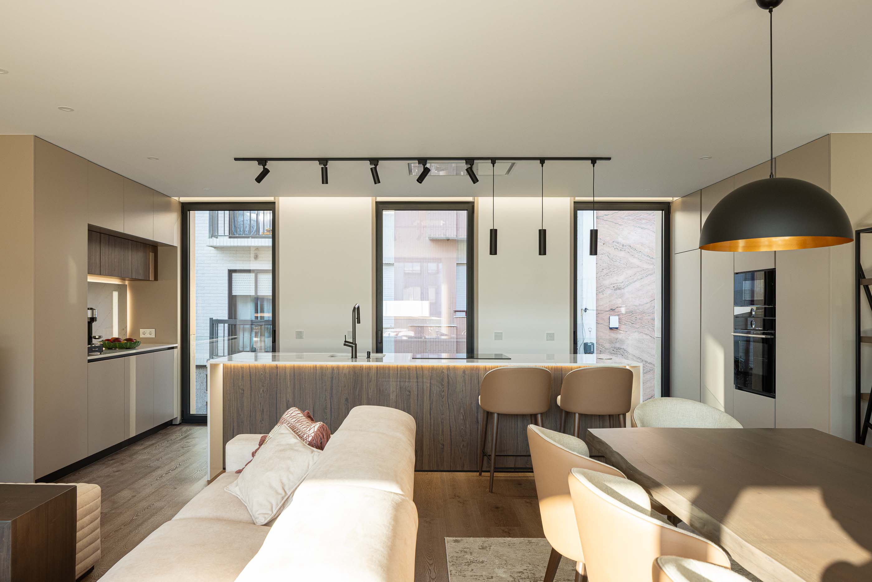 Sala de estar: Espaço amplo com cozinha integrada, ilha central, sofás e mesa de jantar. — Reabilitação Poveira - Edifício FS11 arquitetura Urbanpolis em Póvoa de Varzim