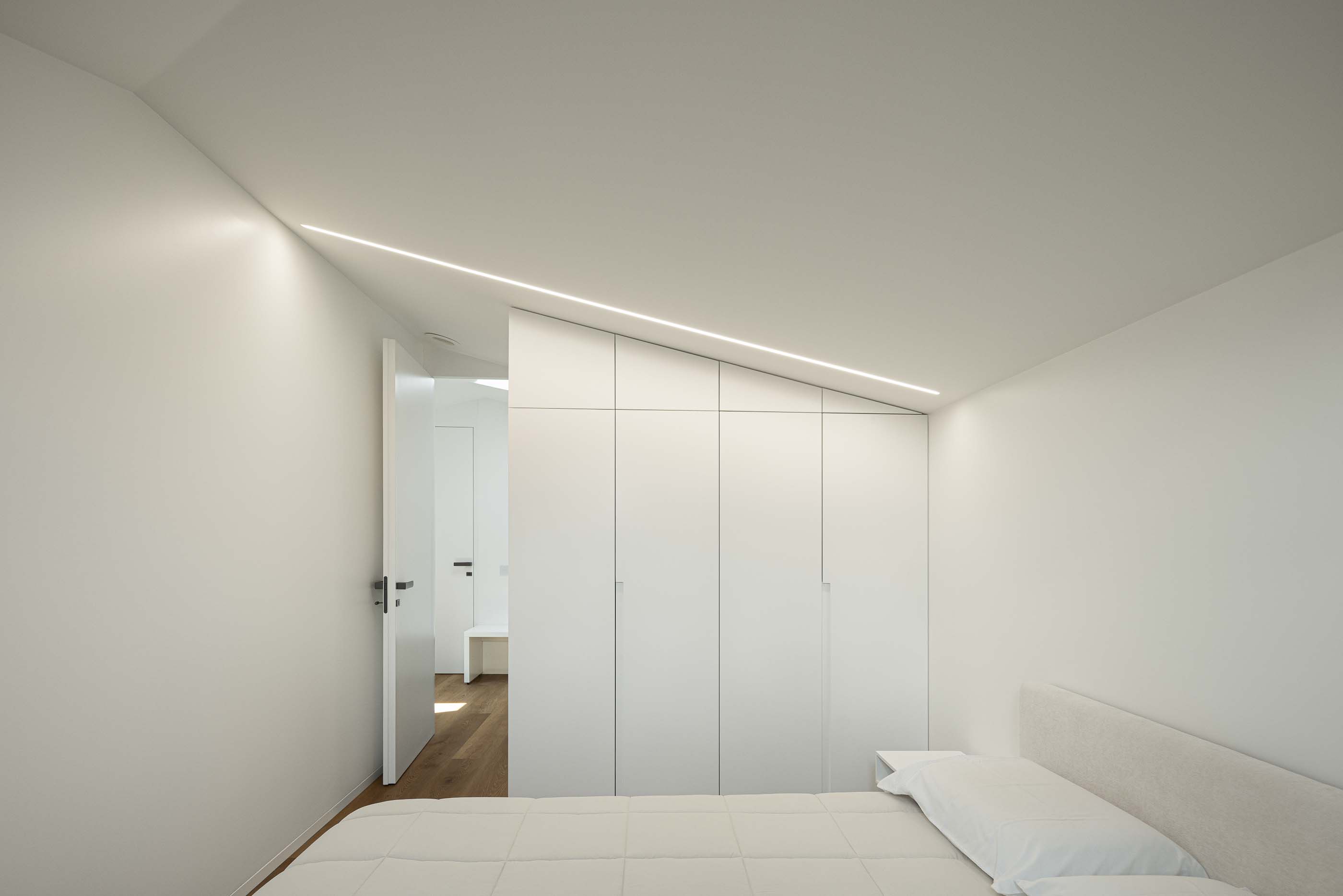 Quarto: Quarto minimalista com armários embutidos, pavimento em madeira e iluminação indireta. — Reabilitação Poveira - Edifício FS11 arquitetura Urbanpolis em Póvoa de Varzim