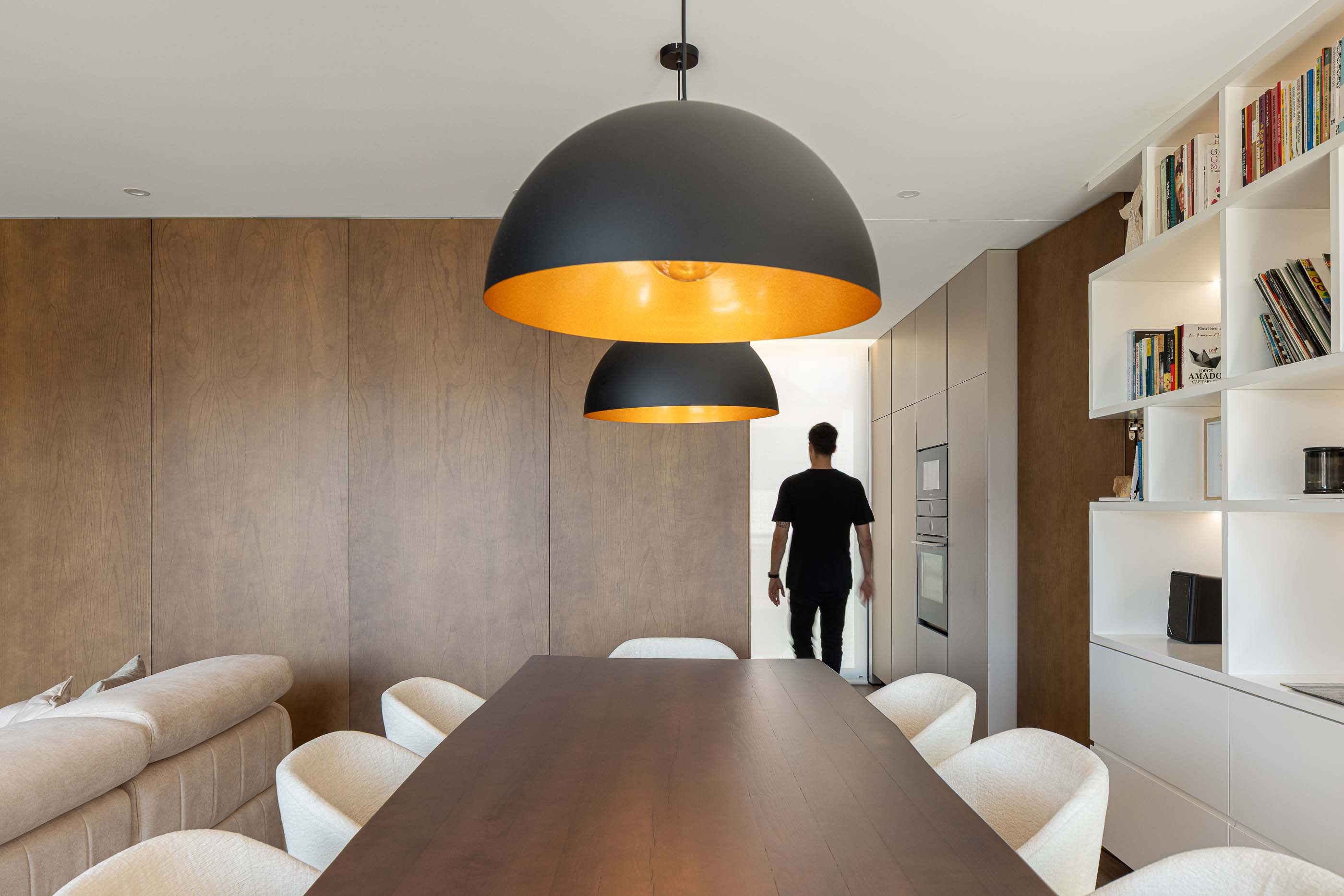 Sala de estar: Mesa de jantar com cadeiras brancas, candeeiros suspensos e estantes embutidas. — Reabilitação Poveira - Edifício FS11 arquitetura Urbanpolis em Póvoa de Varzim