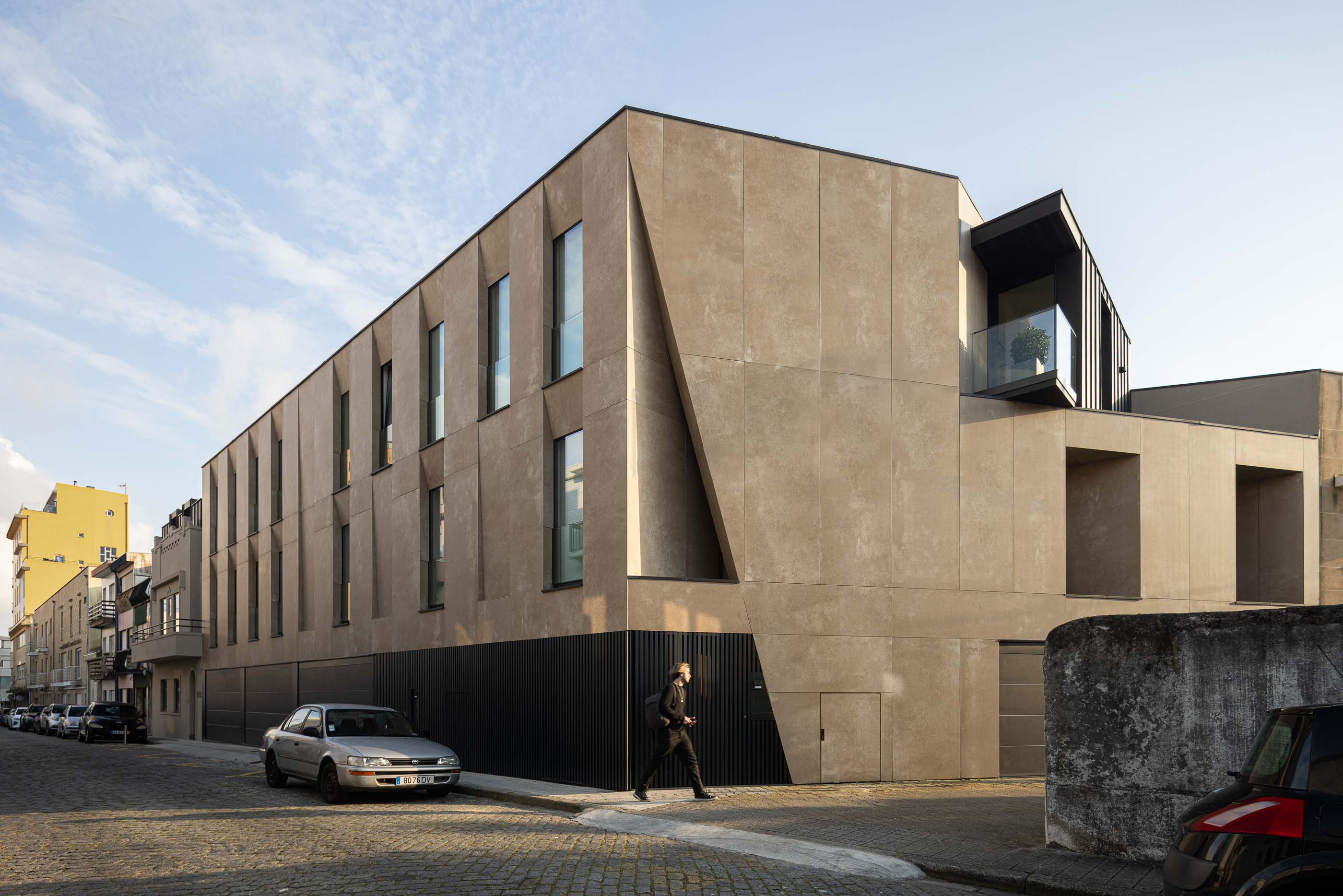 Fachada: Edifício moderno com fachada em tons terra, janelas verticais e detalhes geométricos. — Reabilitação Poveira - Edifício FS11 arquitetura Urbanpolis em Póvoa de Varzim