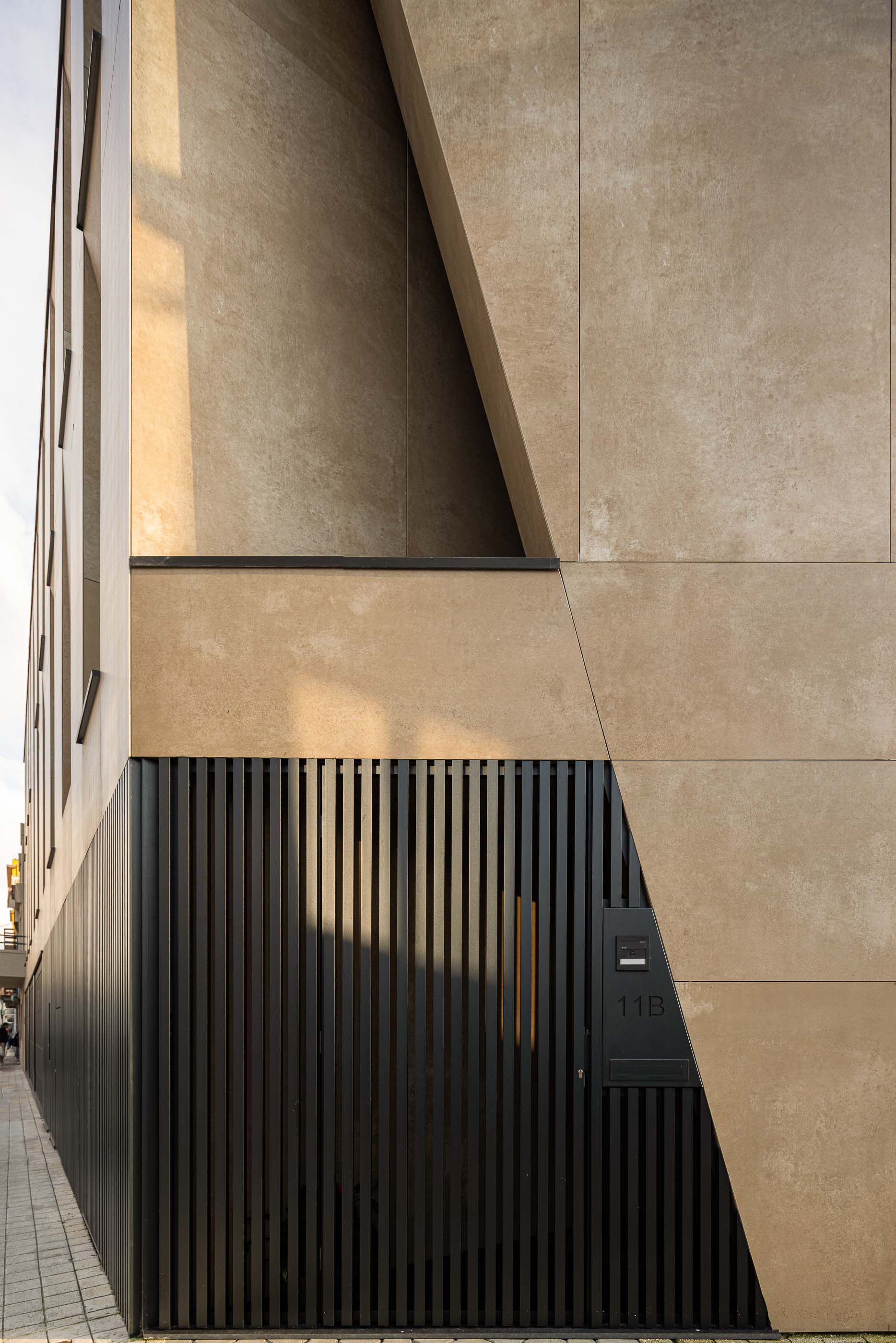 Entrada: Detalhe da entrada com porta preta, fachada em betão e número da casa. — Reabilitação Poveira - Edifício FS11 arquitetura Urbanpolis em Póvoa de Varzim