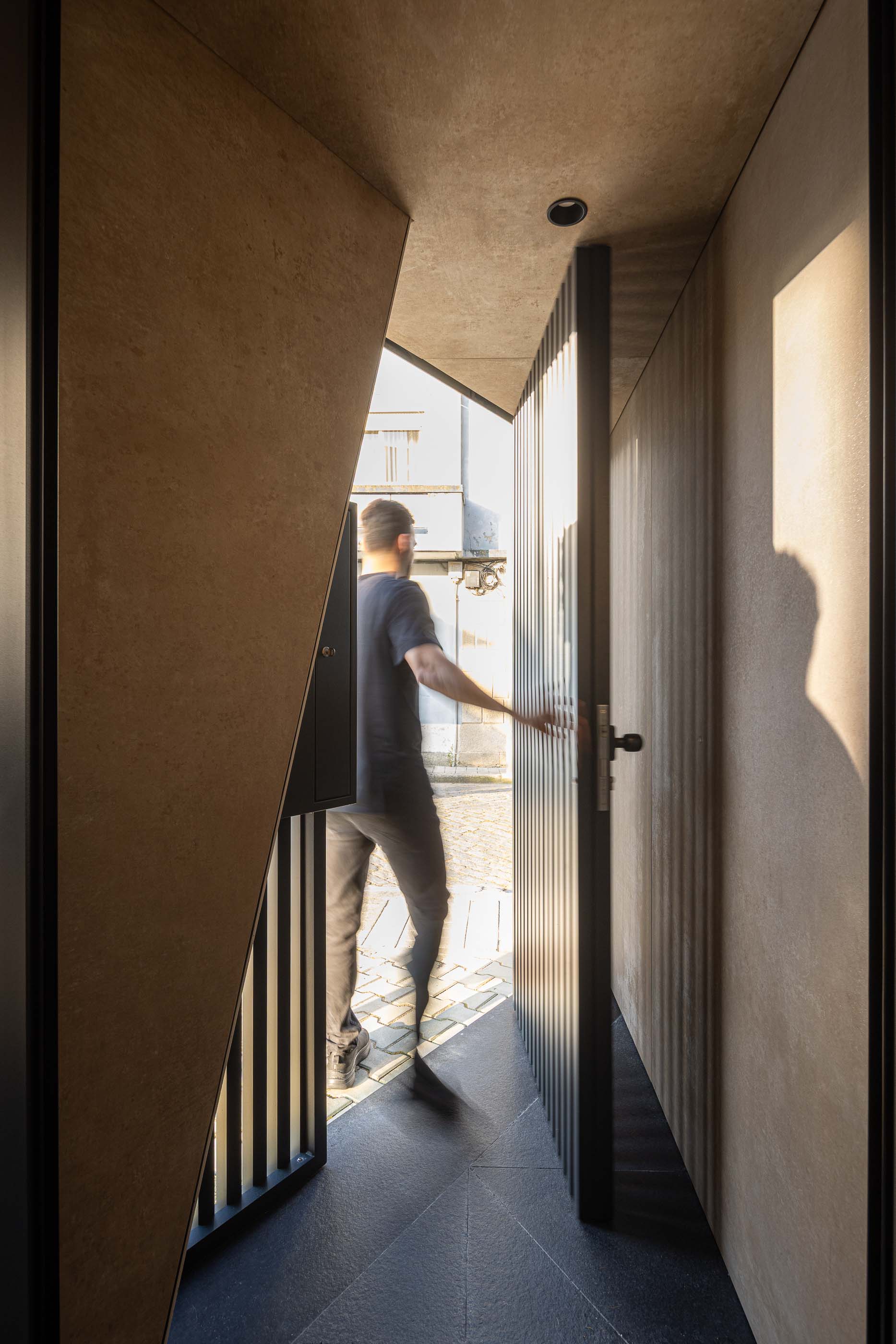 Entrada: Porta de entrada com design moderno, fachada em betão e pavimento em pedra. — Reabilitação Poveira - Edifício FS11 arquitetura Urbanpolis em Póvoa de Varzim