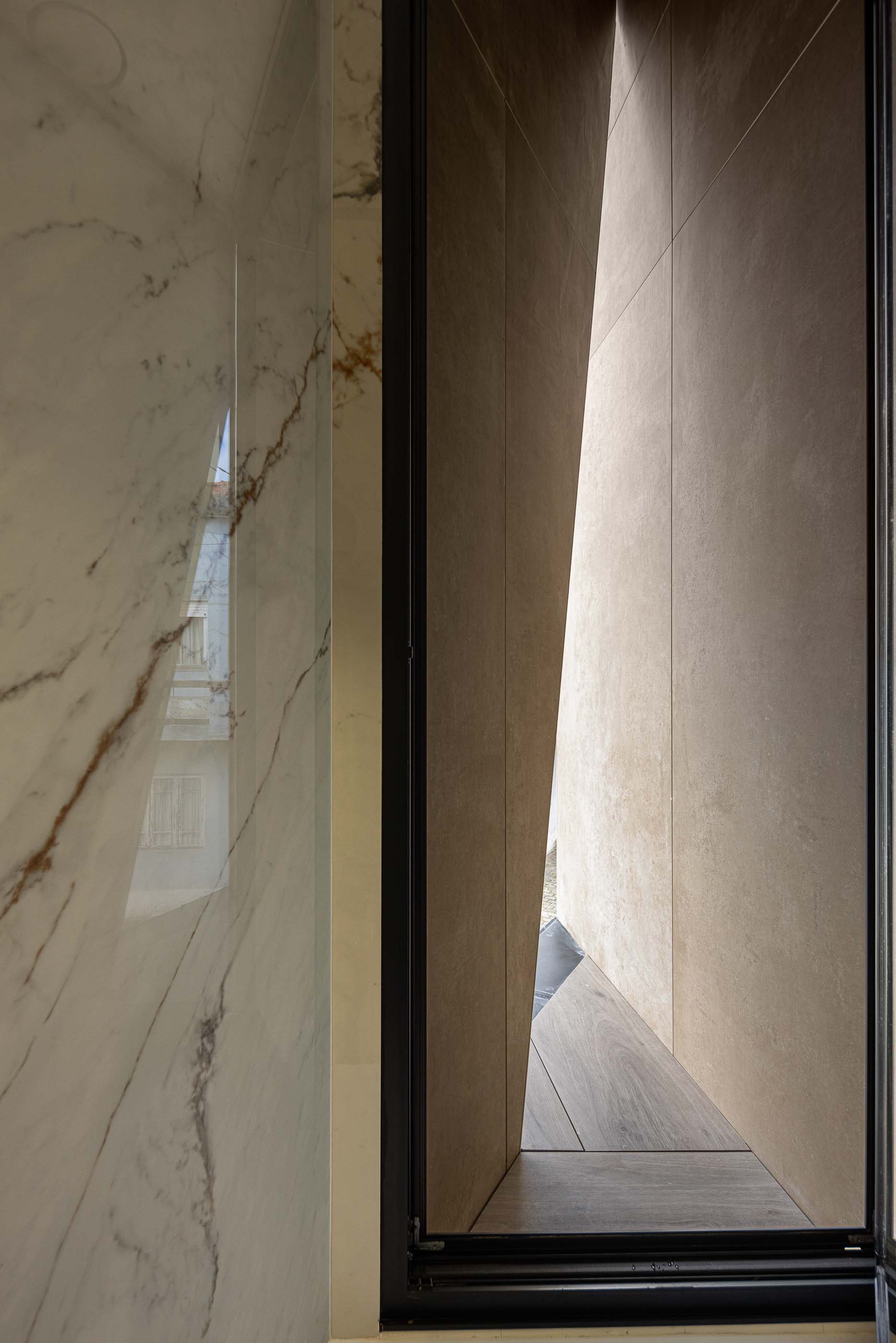 Hall de entrada: Detalhe da porta de vidro, parede em mármore e pavimento em madeira. — Reabilitação Poveira - Edifício FS11 arquitetura Urbanpolis em Póvoa de Varzim