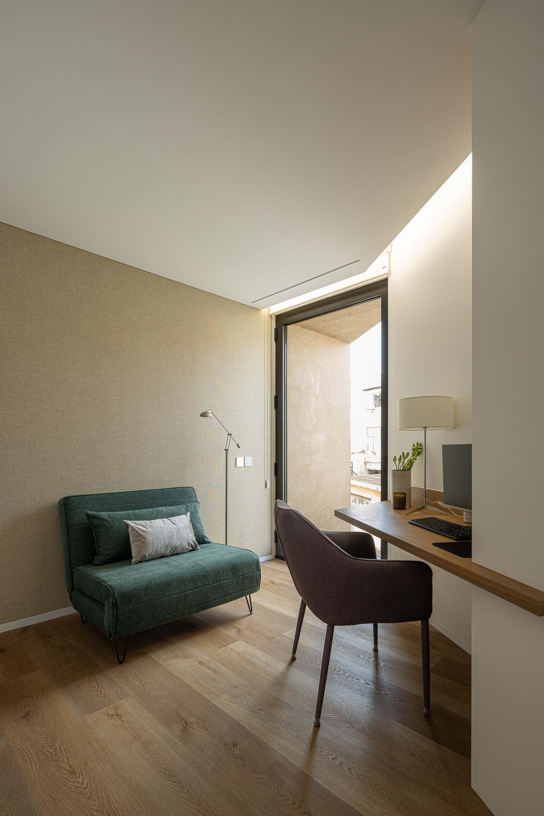 Escritório: Escritório com secretária, cadeira e sofá verde, pavimento em madeira. — Reabilitação Poveira - Edifício FS11 arquitetura Urbanpolis em Póvoa de Varzim