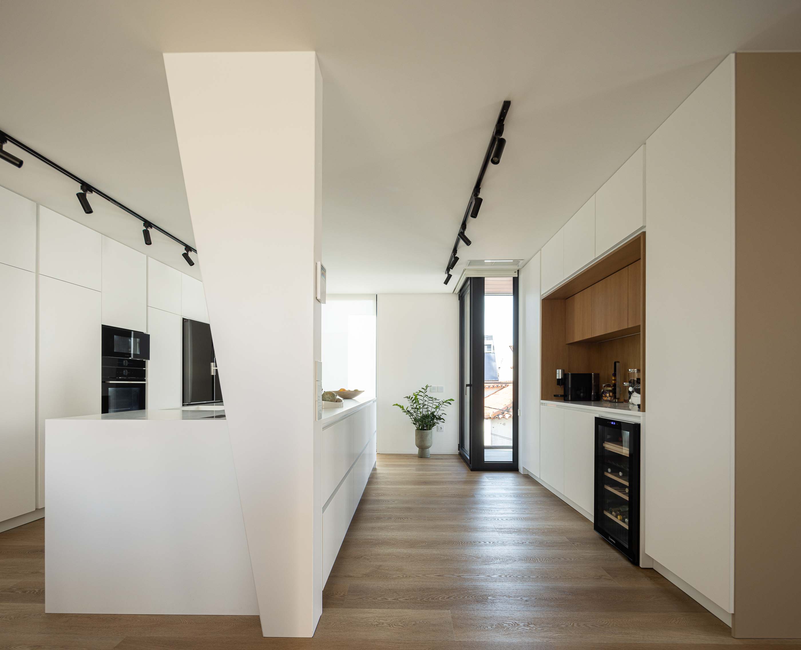 Cozinha: Cozinha moderna com ilha central, armários brancos e pavimento em madeira. — Reabilitação Poveira - Edifício FS11 arquitetura Urbanpolis em Póvoa de Varzim