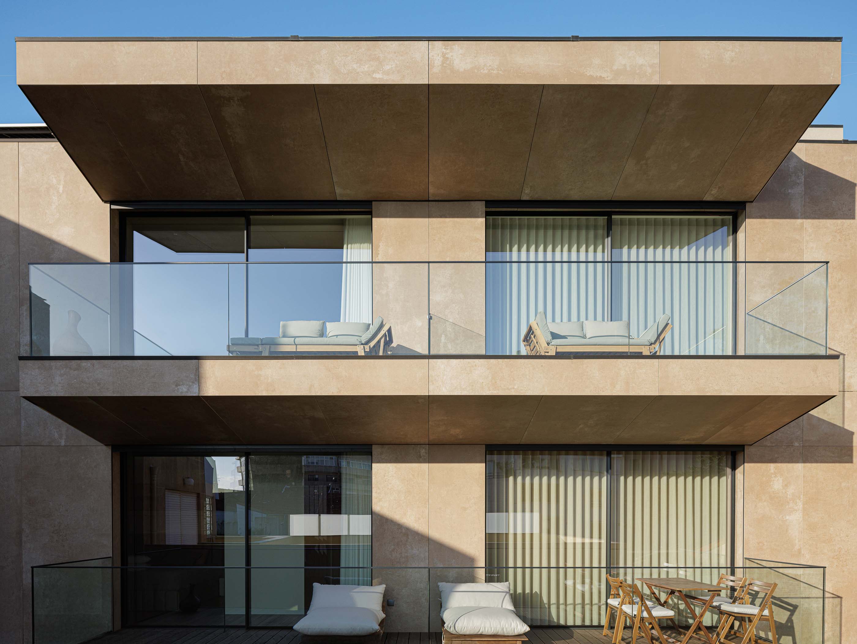 Varanda: Varandas com sofás e cadeiras, pavimento em madeira e guarda em vidro. — Reabilitação Poveira - Edifício FS11 arquitetura Urbanpolis em Póvoa de Varzim