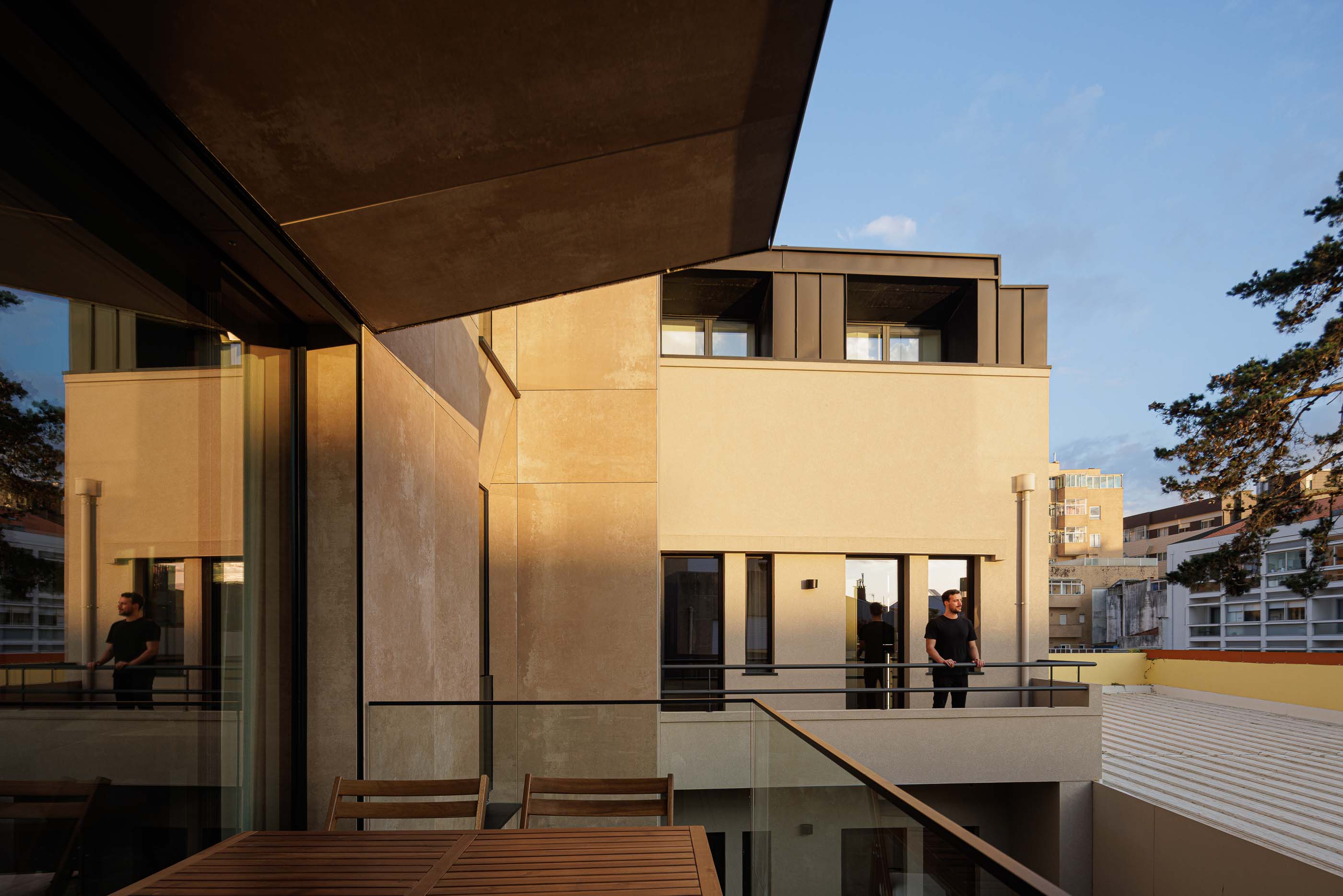 Varanda: Varanda com mesa e cadeiras, pavimento em madeira e vista para o exterior. — Reabilitação Poveira - Edifício FS11 arquitetura Urbanpolis em Póvoa de Varzim