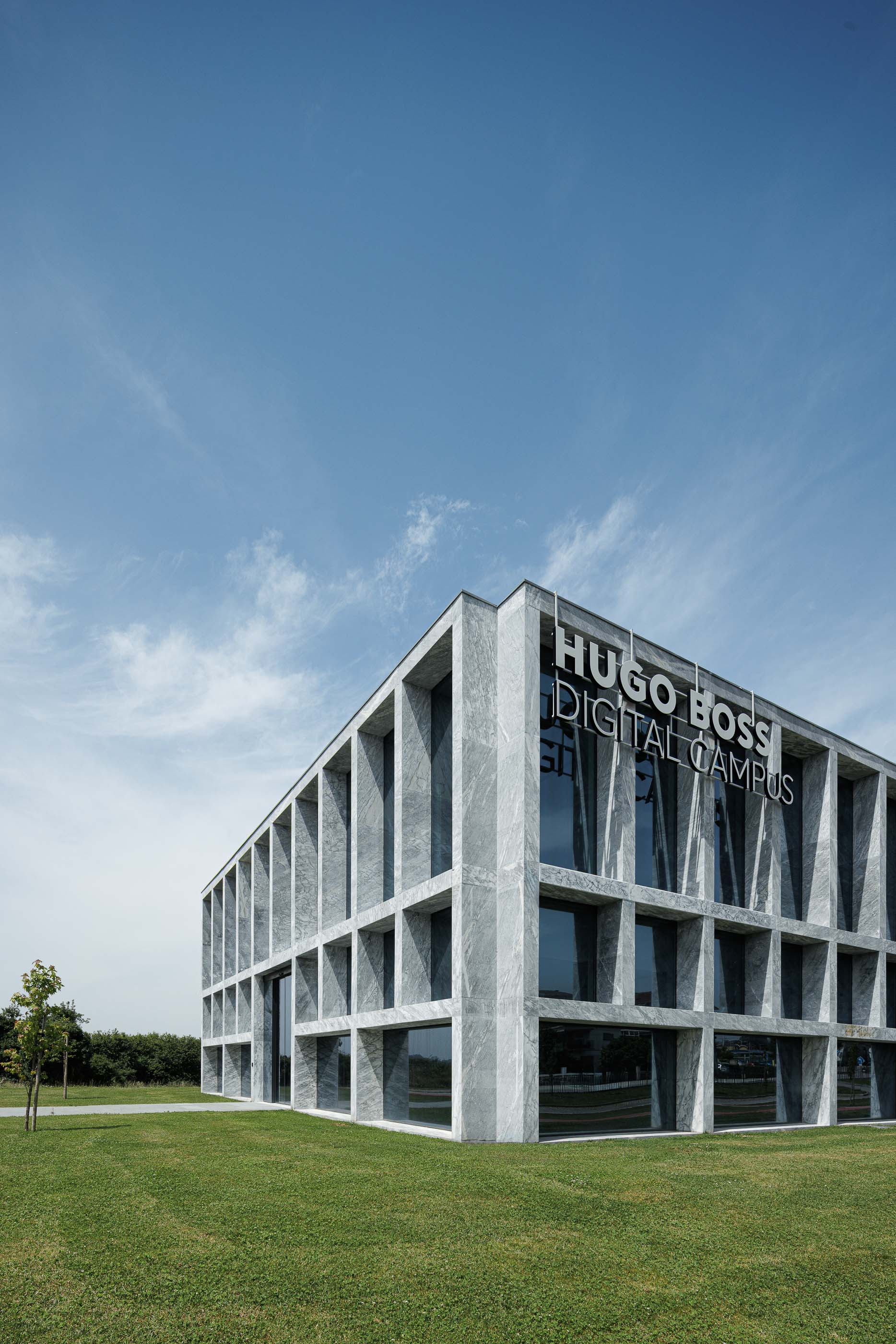 Edifício: Perspectiva angular do edifício Hugo Boss Digital Campus, com fachada em mármore e amplas janelas. — Metyis Digital Campus arquitetura UNUM - Oficina de Arquitetura em Gondomar