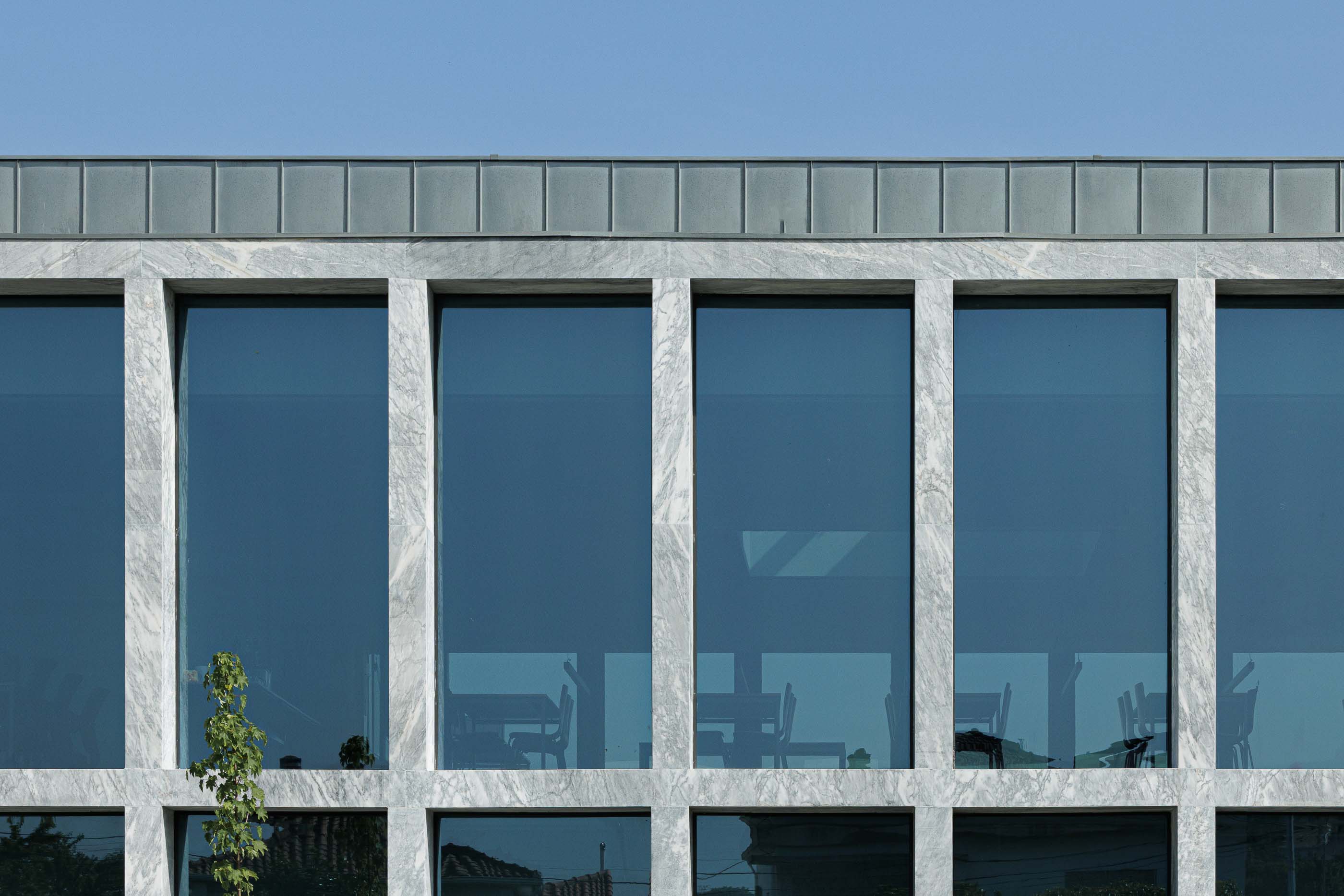 Edifício: Close-up da fachada em mármore com janelas, revelando mobiliário de escritório no interior. — Metyis Digital Campus arquitetura UNUM - Oficina de Arquitetura em Gondomar