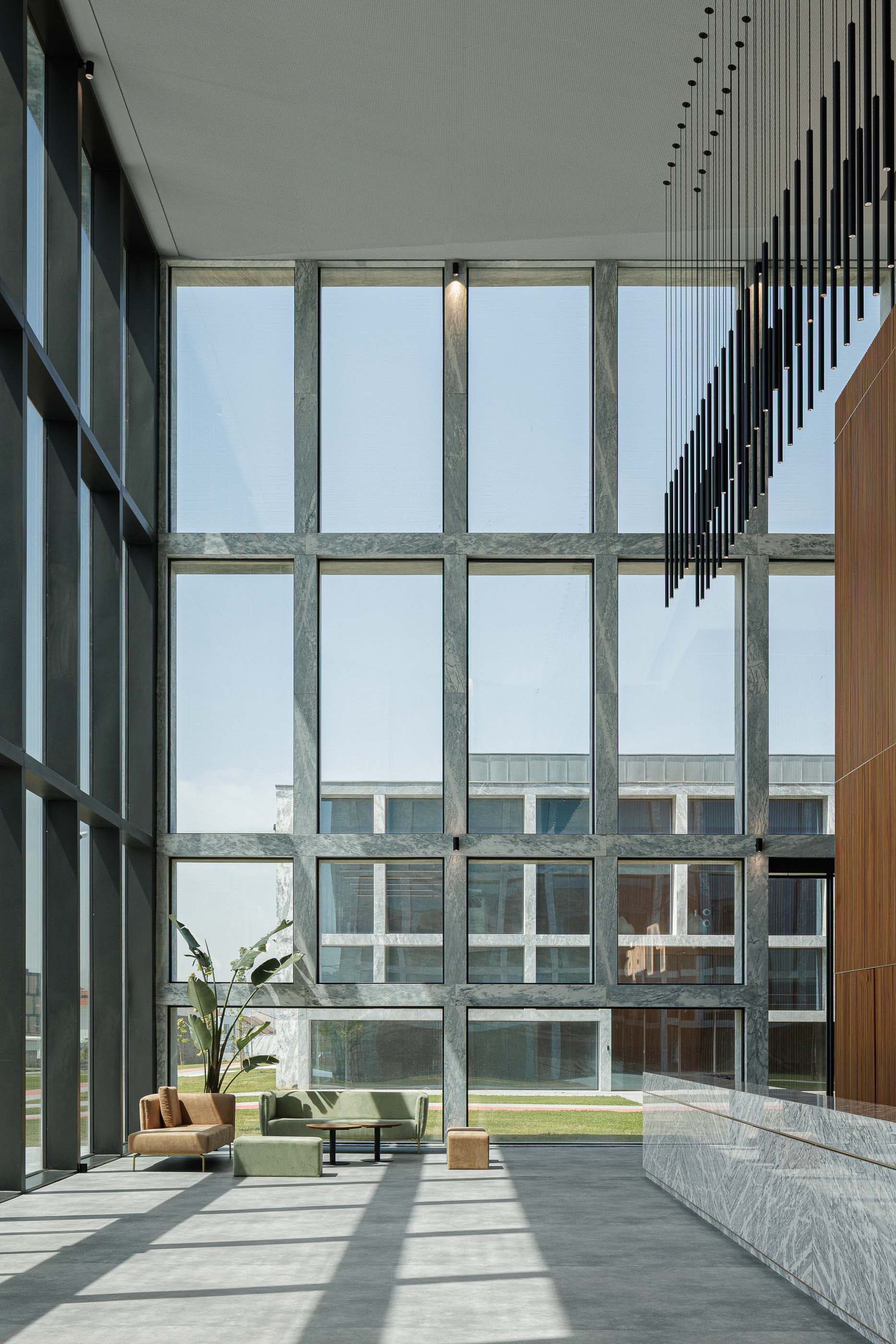 Hall de entrada: Espaço amplo com janelas altas, pavimento em cimento afagado, candeeiros suspensos e mobiliário minimalista. — Metyis Digital Campus arquitetura UNUM - Oficina de Arquitetura em Gondomar