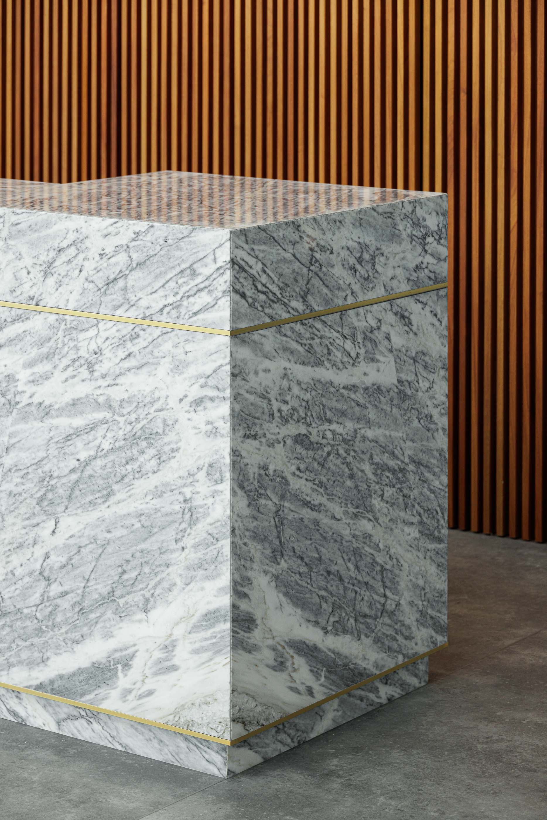 Hall de entrada: Detalhe do balcão de recepção em mármore com detalhes em dourado e parede em madeira ripada. — Metyis Digital Campus arquitetura UNUM - Oficina de Arquitetura em Gondomar