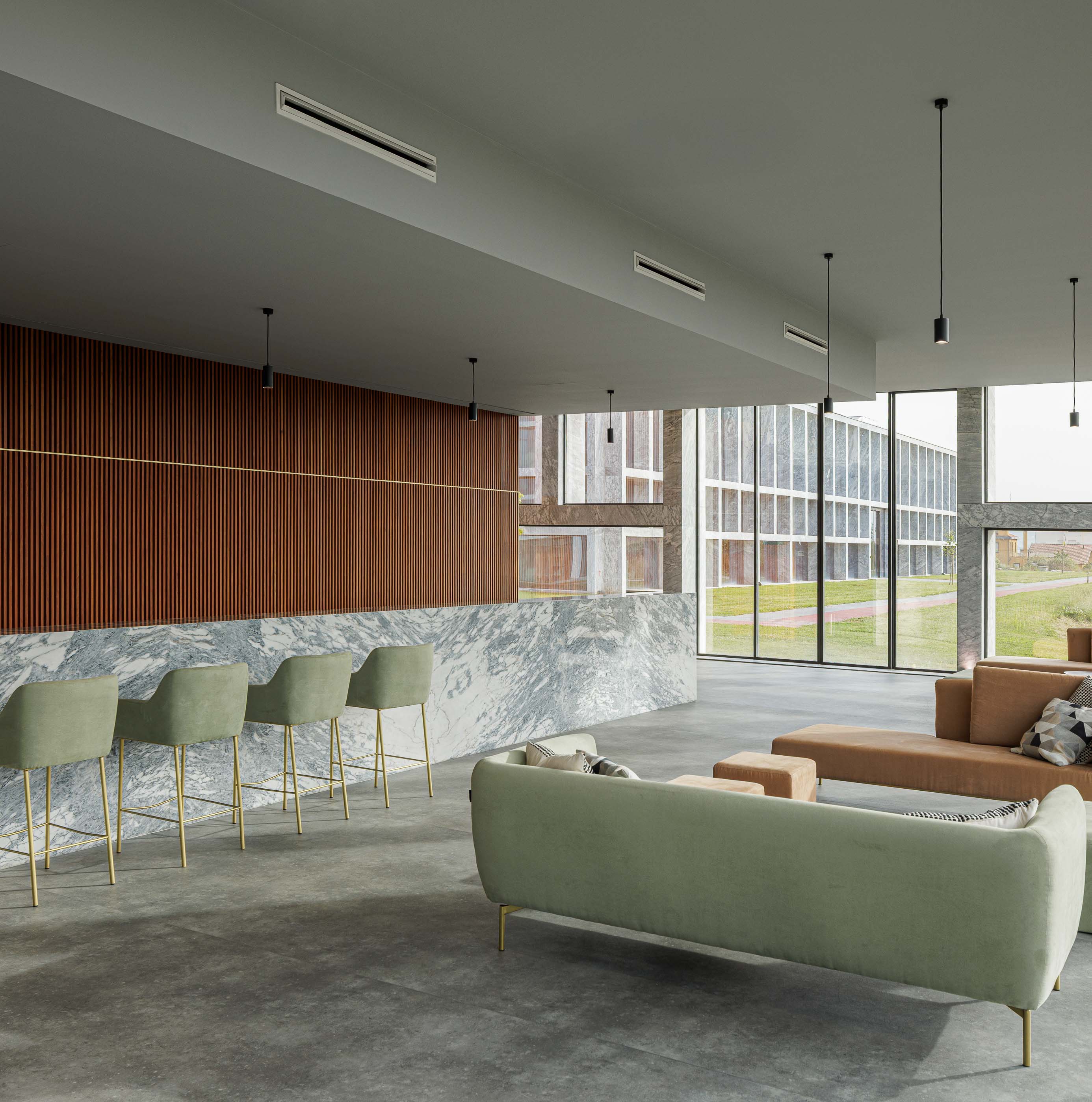 Cafetaria: Espaço de cafetaria com balcão em mármore, cadeiras altas, sofás e pavimento em cimento afagado. — Metyis Digital Campus arquitetura UNUM - Oficina de Arquitetura em Gondomar