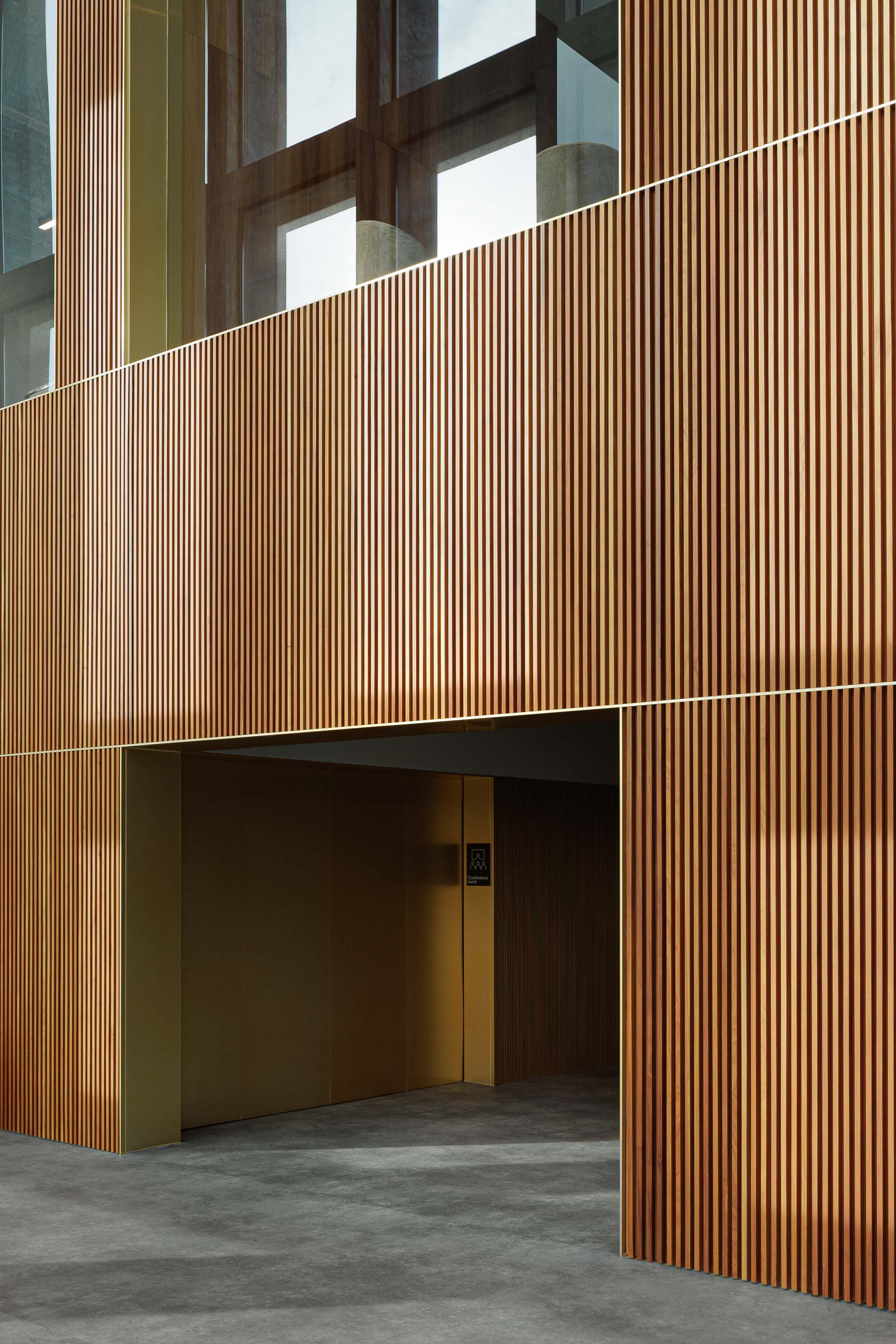 Corredor: Detalhe de paredes em madeira ripada com detalhes em dourado e porta de acesso ao elevador. — Metyis Digital Campus arquitetura UNUM - Oficina de Arquitetura em Gondomar