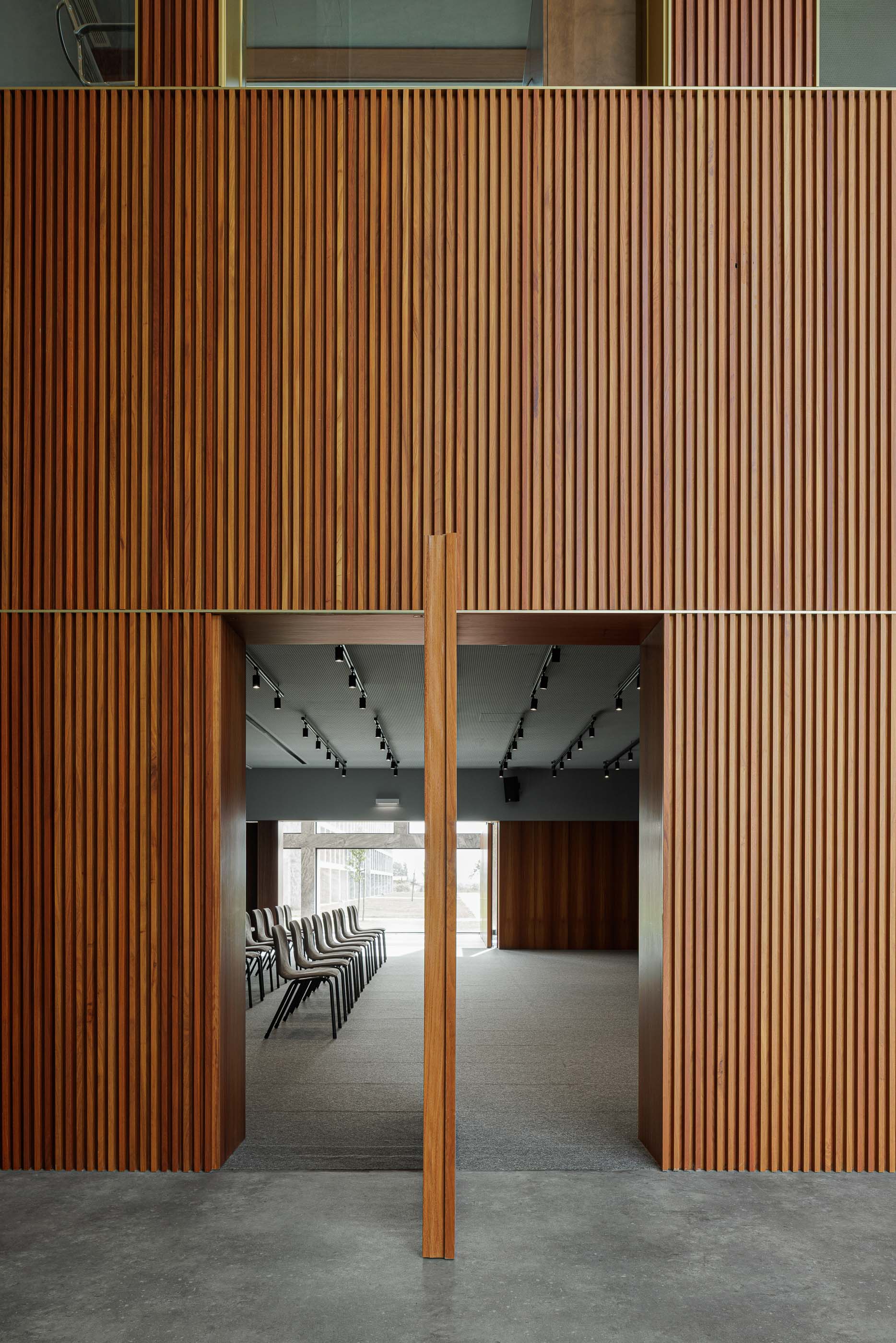 Sala de reuniões: Entrada para sala de reuniões com paredes em madeira ripada e alcatifa no interior. — Metyis Digital Campus arquitetura UNUM - Oficina de Arquitetura em Gondomar