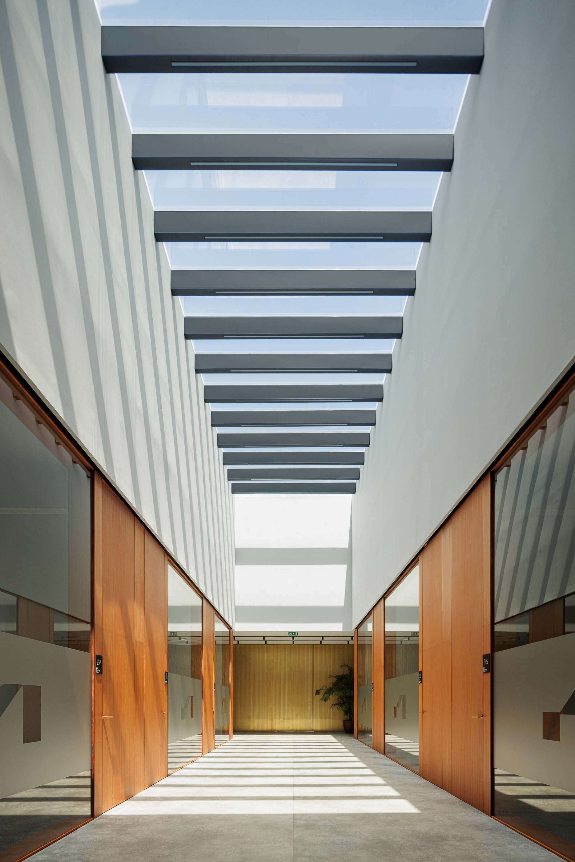 Corredor: Corredor iluminado por claraboia, com portas de madeira e sinalização nos escritórios. — Metyis Digital Campus arquitetura UNUM - Oficina de Arquitetura em Gondomar