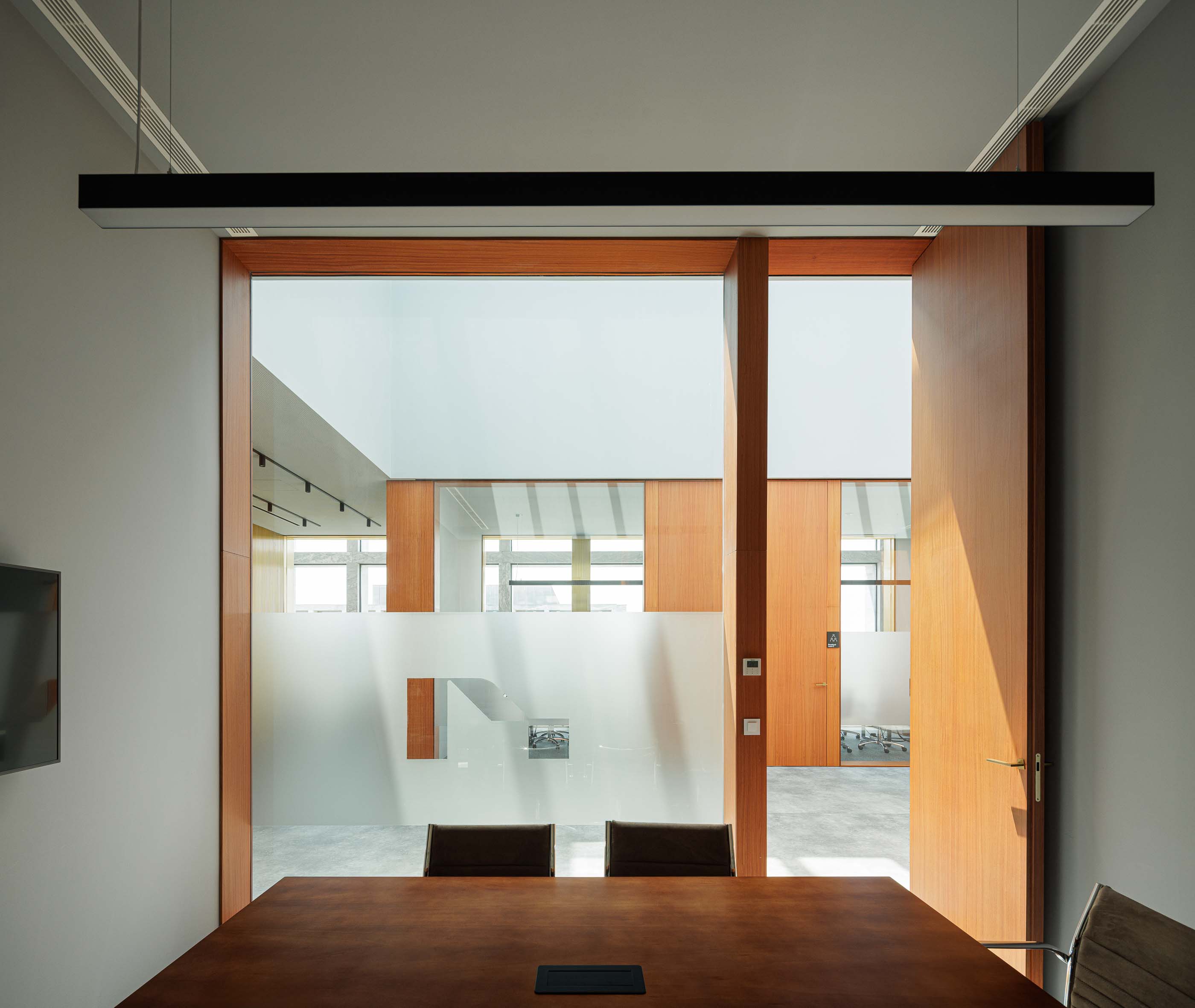 Escritório: Vista de um escritório através de uma porta de madeira, com mesa de reuniões e cadeiras. — Metyis Digital Campus arquitetura UNUM - Oficina de Arquitetura em Gondomar