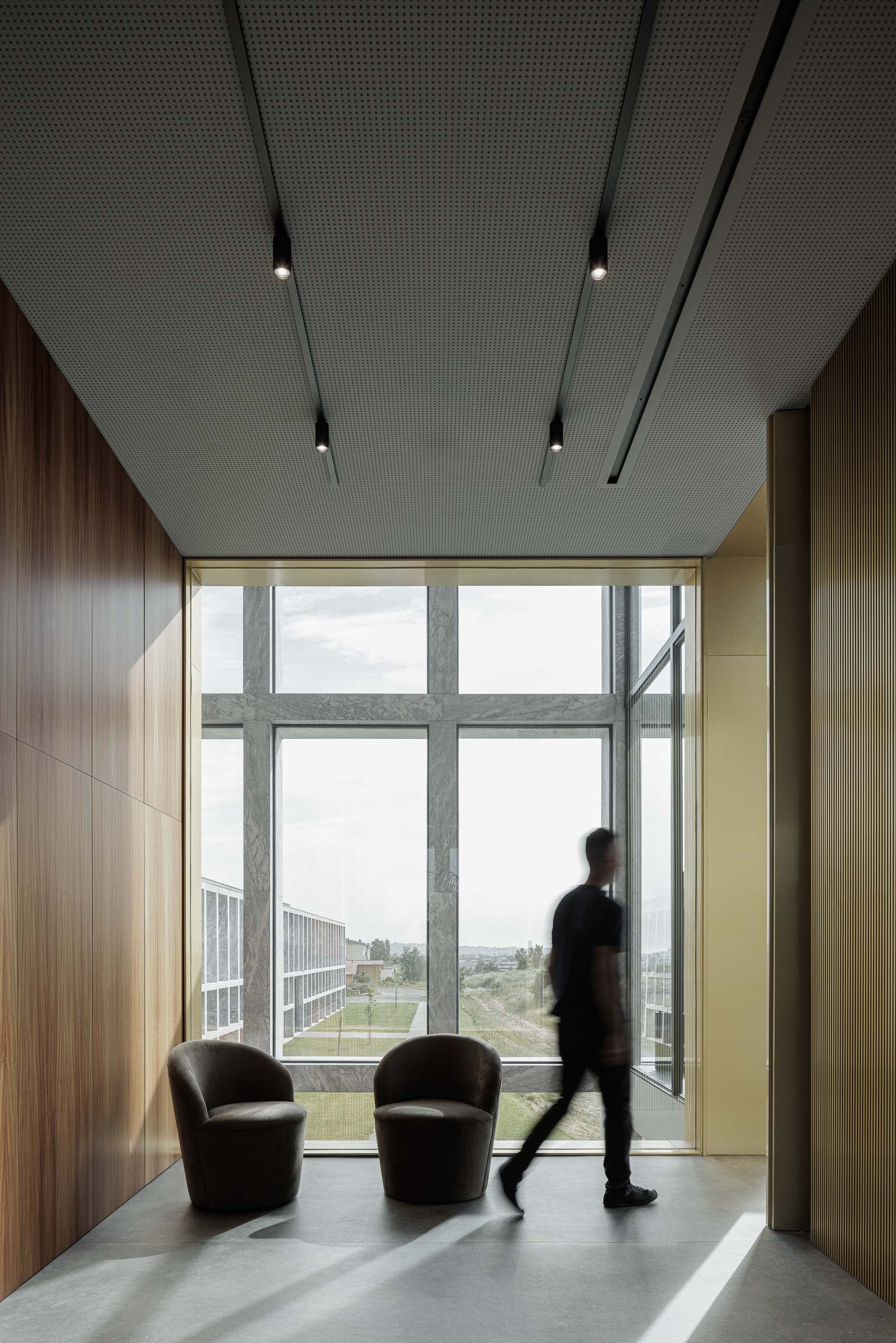 Espaço de trabalho: Corredor com cadeirões e vista para o exterior, com paredes em madeira e iluminação embutida. — Metyis Digital Campus arquitetura UNUM - Oficina de Arquitetura em Gondomar