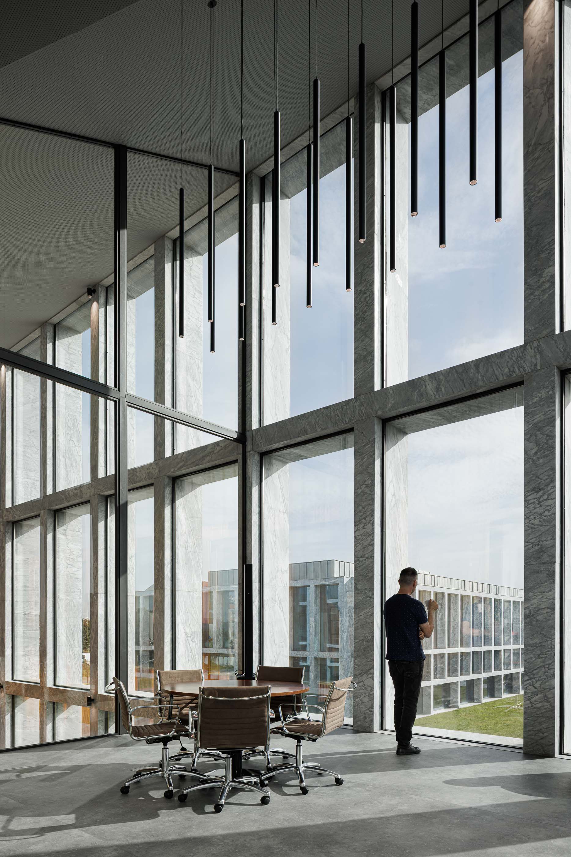 Escritório: Espaço de escritório com mesa de reuniões, cadeiras, candeeiros suspensos e vista para o exterior. — Metyis Digital Campus arquitetura UNUM - Oficina de Arquitetura em Gondomar