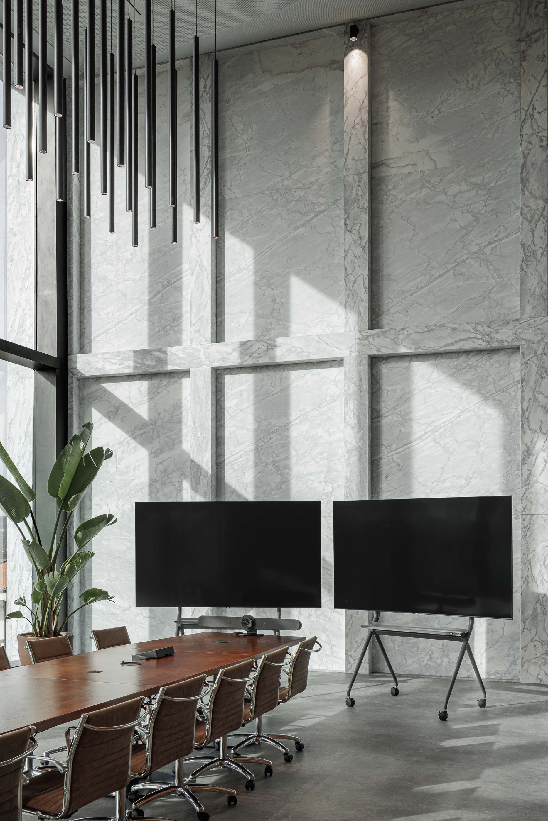 Escritório: Sala de reuniões com mesa comprida, cadeiras, duas telas e parede em mármore. — Metyis Digital Campus arquitetura UNUM - Oficina de Arquitetura em Gondomar