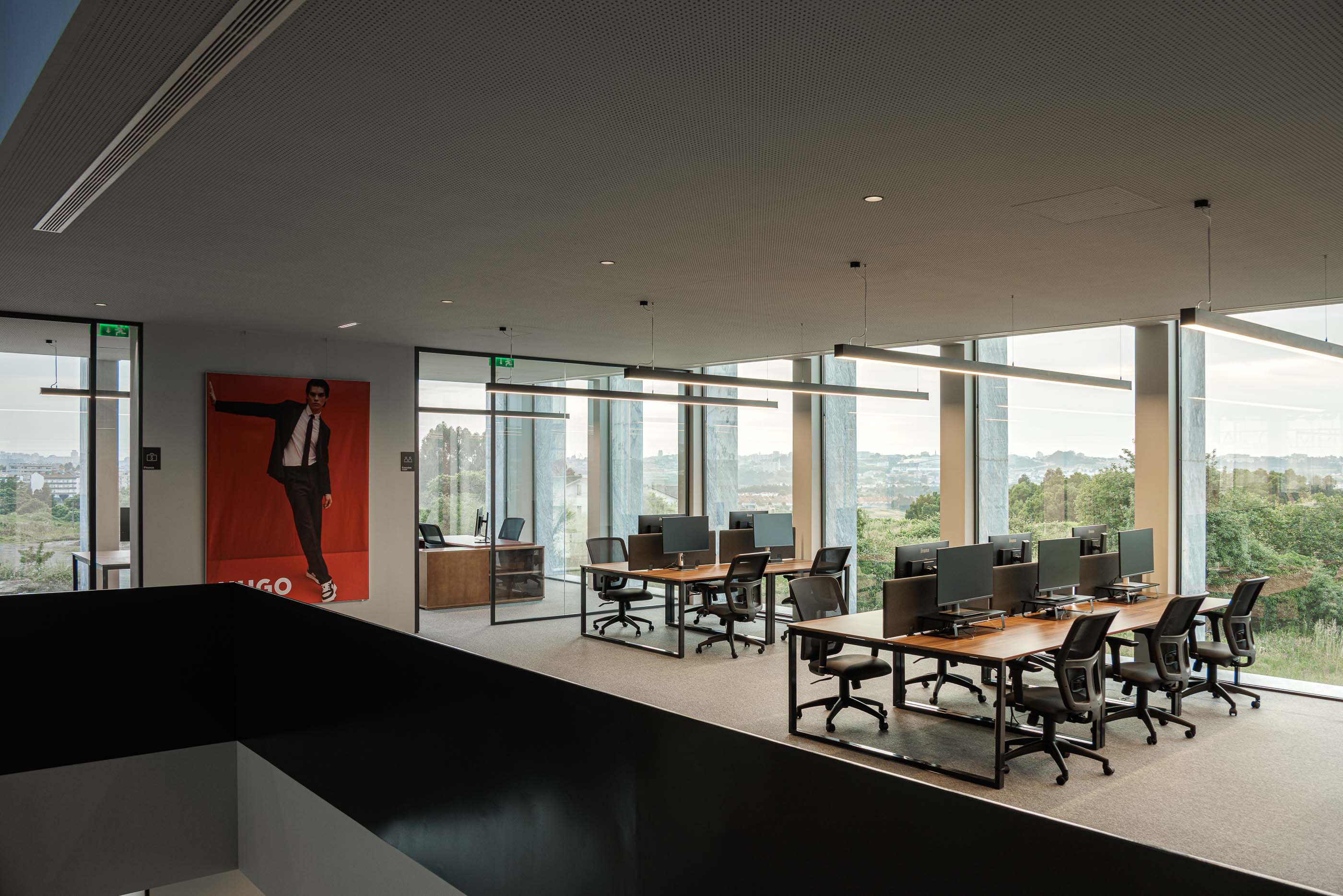 Escritório: Espaço de trabalho com secretárias, cadeiras, computadores e vista para o exterior. — Metyis Digital Campus arquitetura UNUM - Oficina de Arquitetura em Gondomar