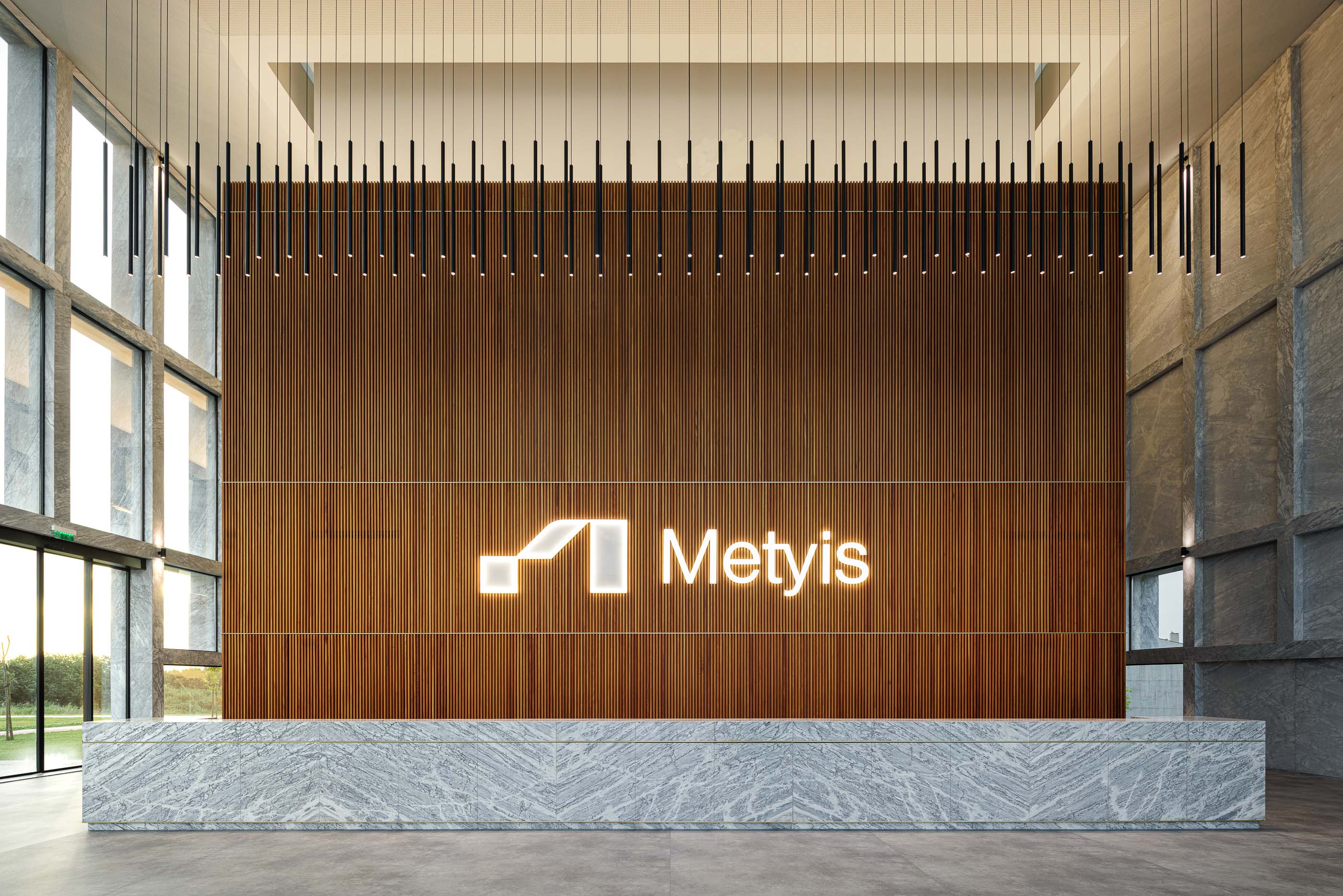 Hall de entrada: Recepção com balcão em mármore, parede em madeira ripada e candeeiros suspensos. — Metyis Digital Campus arquitetura UNUM - Oficina de Arquitetura em Gondomar