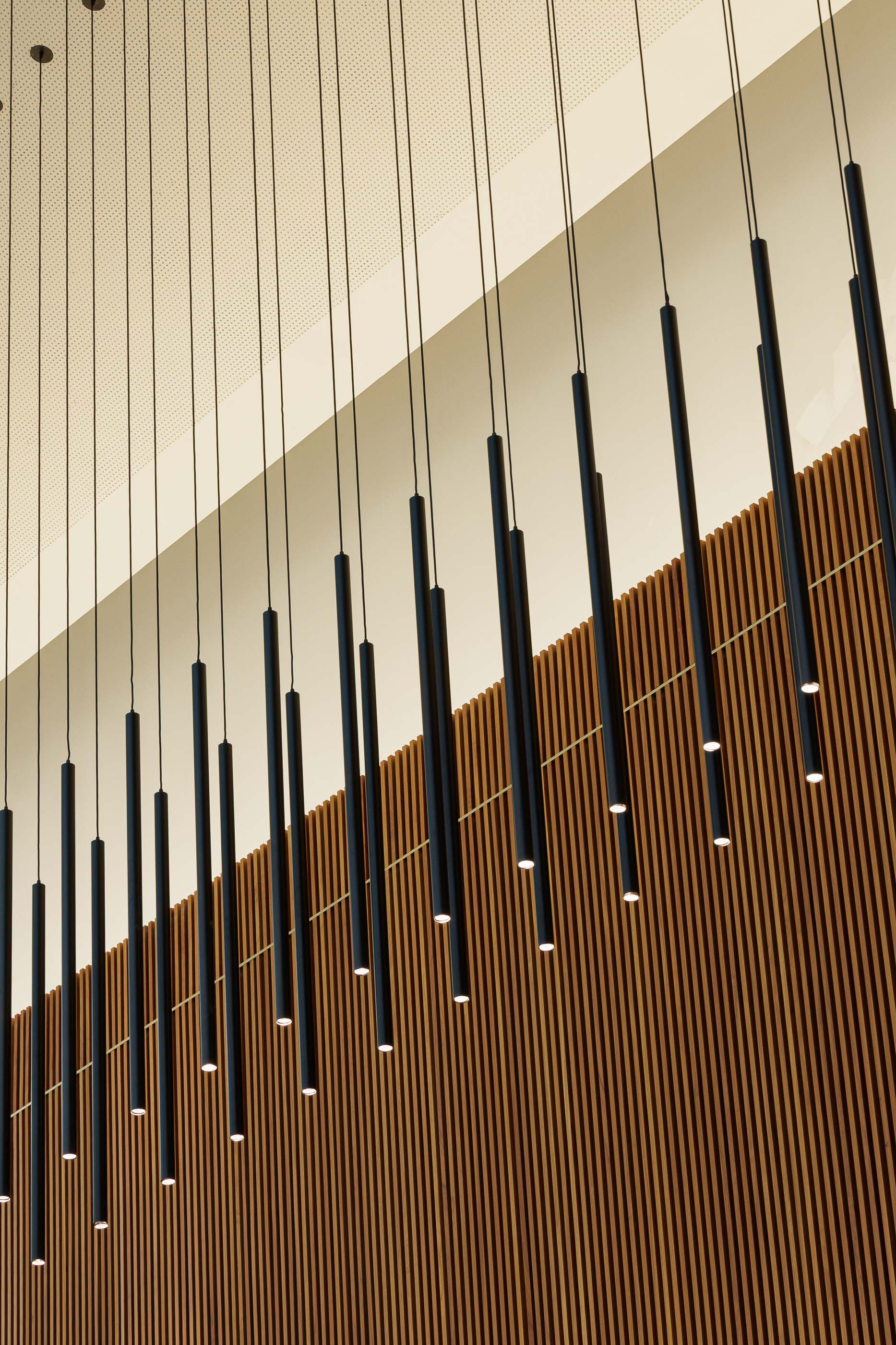 Hall de entrada: Detalhe dos candeeiros suspensos e parede em madeira ripada. — Metyis Digital Campus arquitetura UNUM - Oficina de Arquitetura em Gondomar