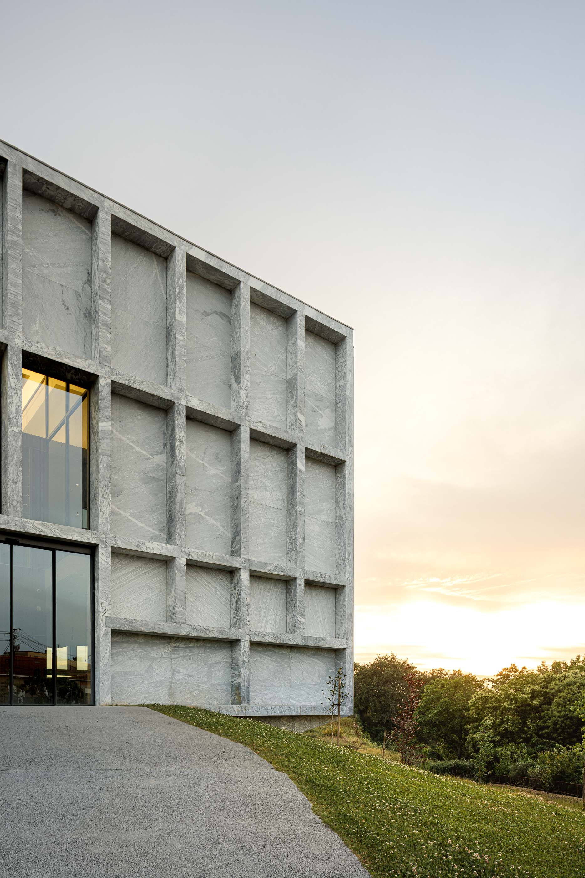 Edifício: Detalhe da fachada em mármore com janelas iluminadas ao entardecer. — Metyis Digital Campus arquitetura UNUM - Oficina de Arquitetura em Gondomar