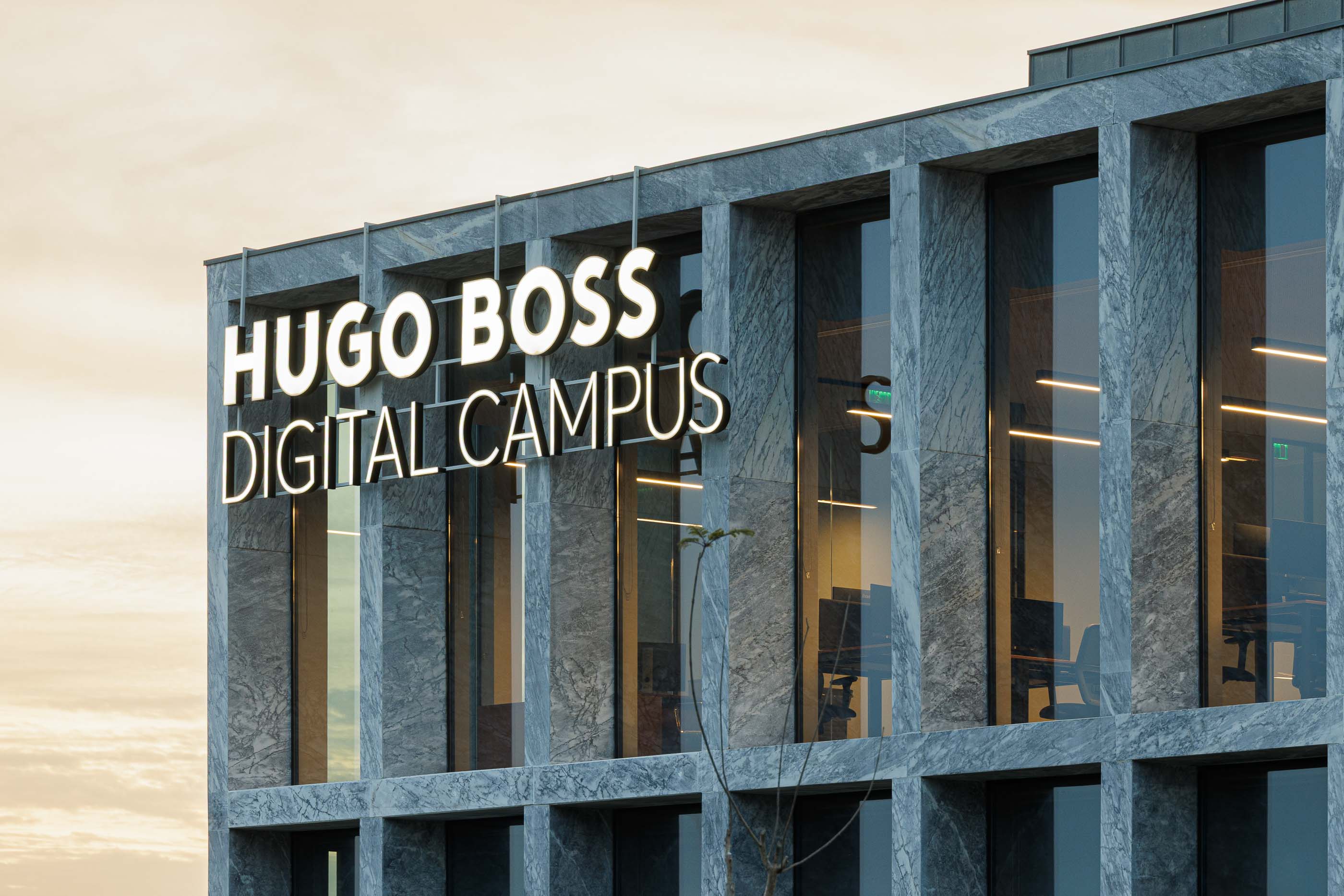 Edifício: Detalhe da fachada em mármore com o logótipo da Hugo Boss Digital Campus iluminado. — Metyis Digital Campus arquitetura UNUM - Oficina de Arquitetura em Gondomar